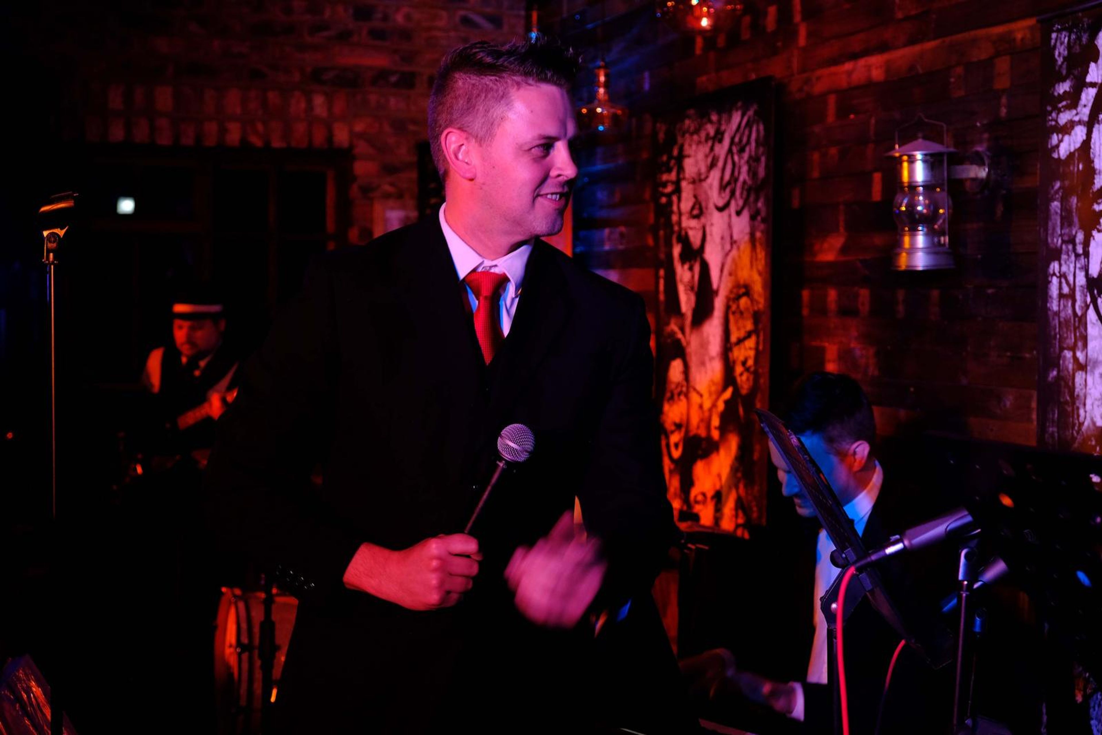 Singer in a suit and red tie holding the microphone, glancing off stage