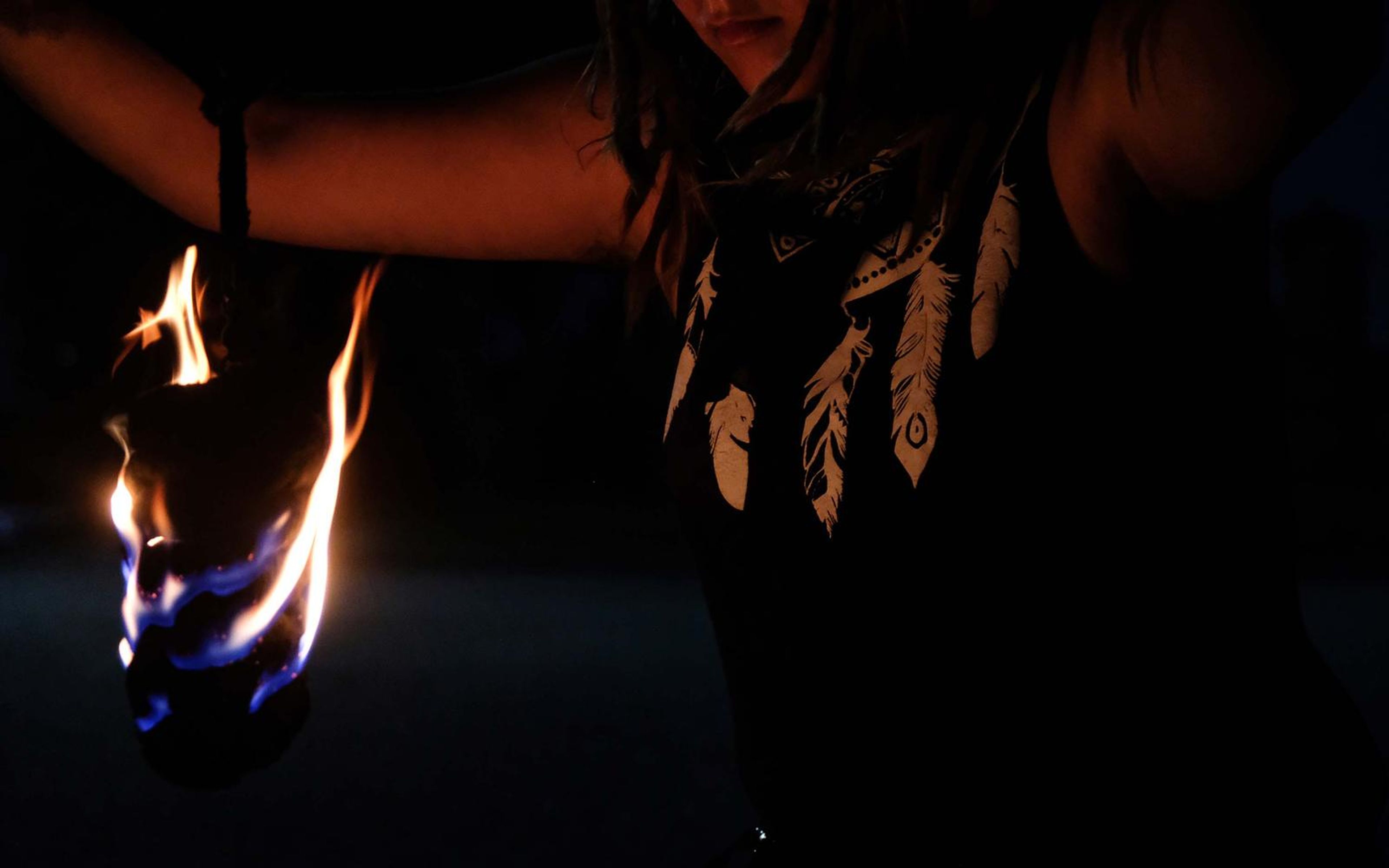 Flame at the left of a feather-print top with one arm stretched out, face out of frame
