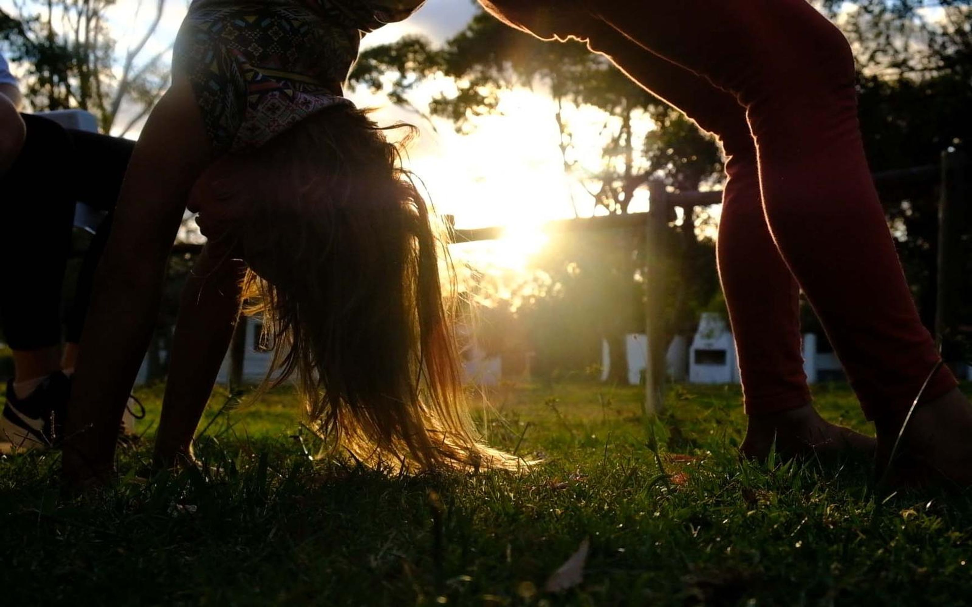 Backlit girl mid-cartwheel on grass with low sun flaring through her hair