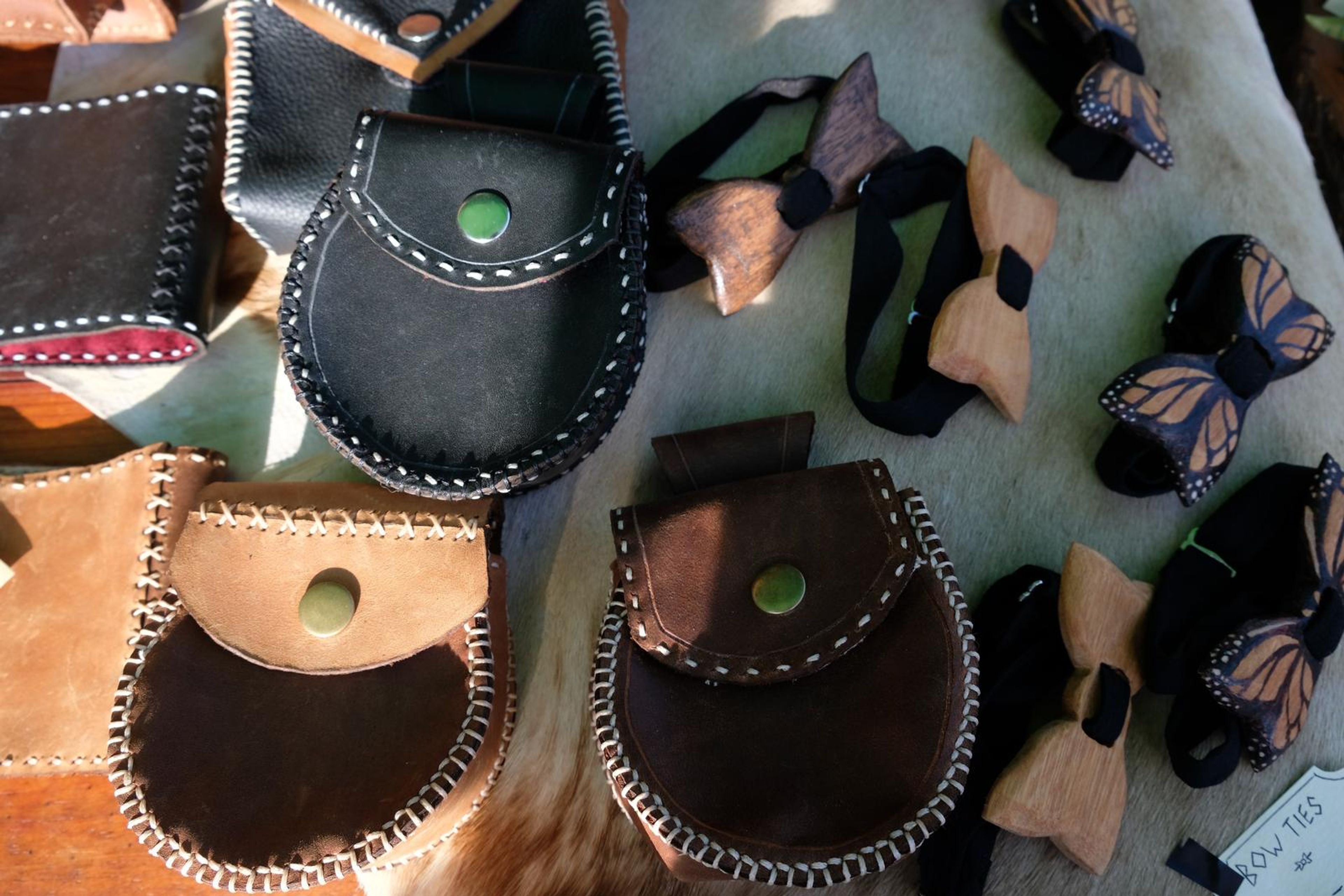 Leather pouches and carved wooden bow ties on a hide from above