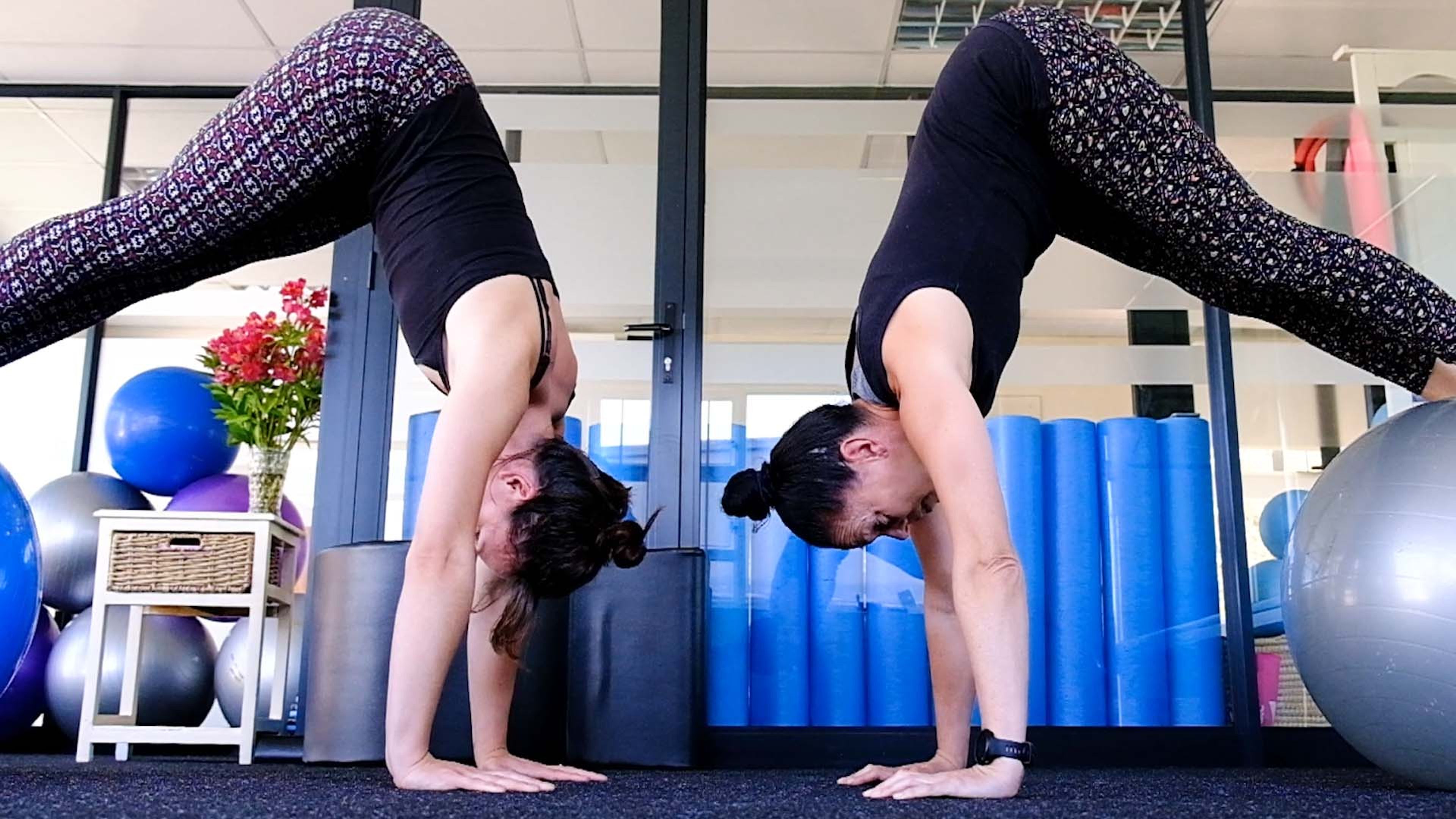 Two women practising inverted poses beside stability balls and foam rollers