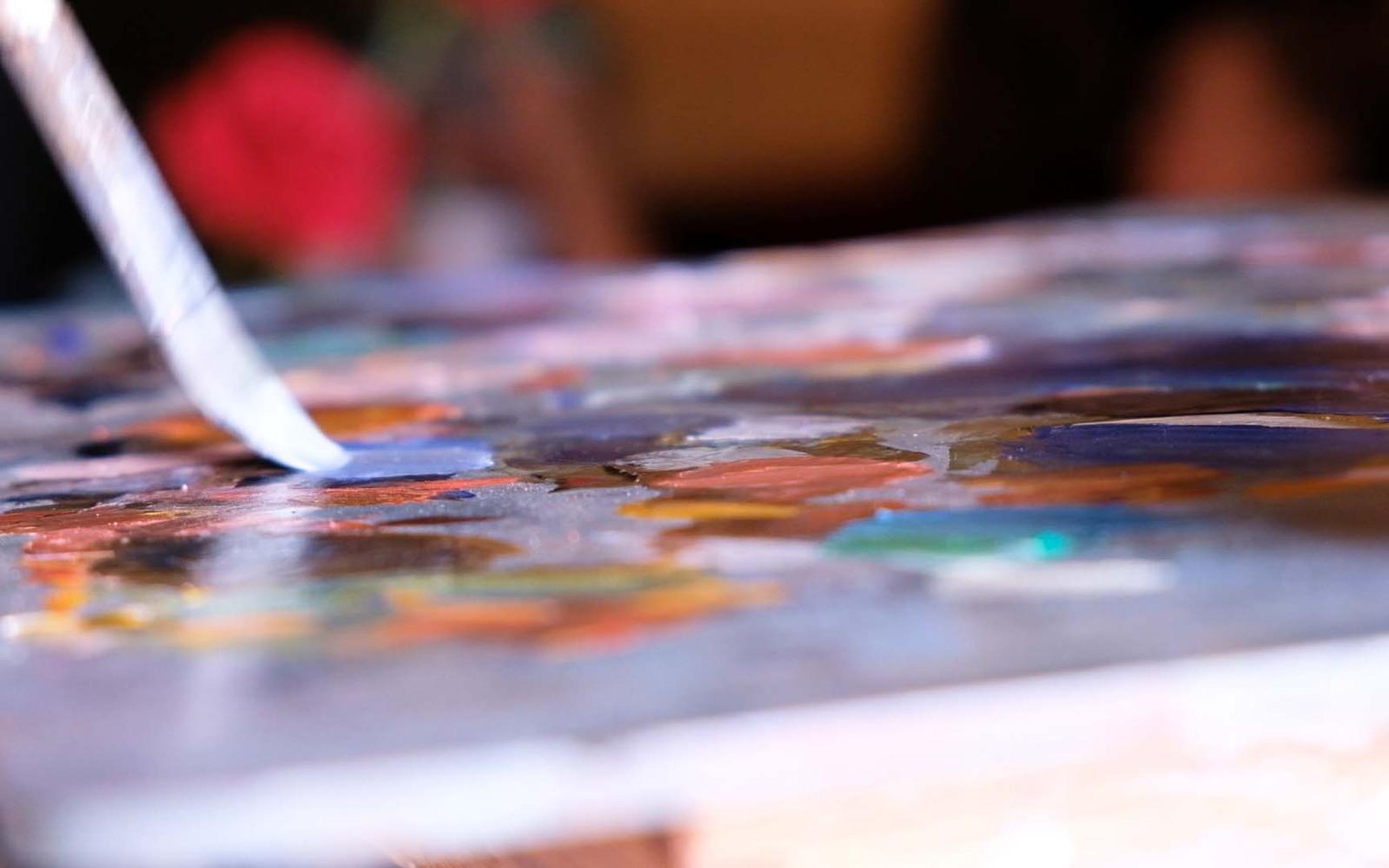 Palette knife touching wet blue paint on a colourful painting palette with a soft focus background