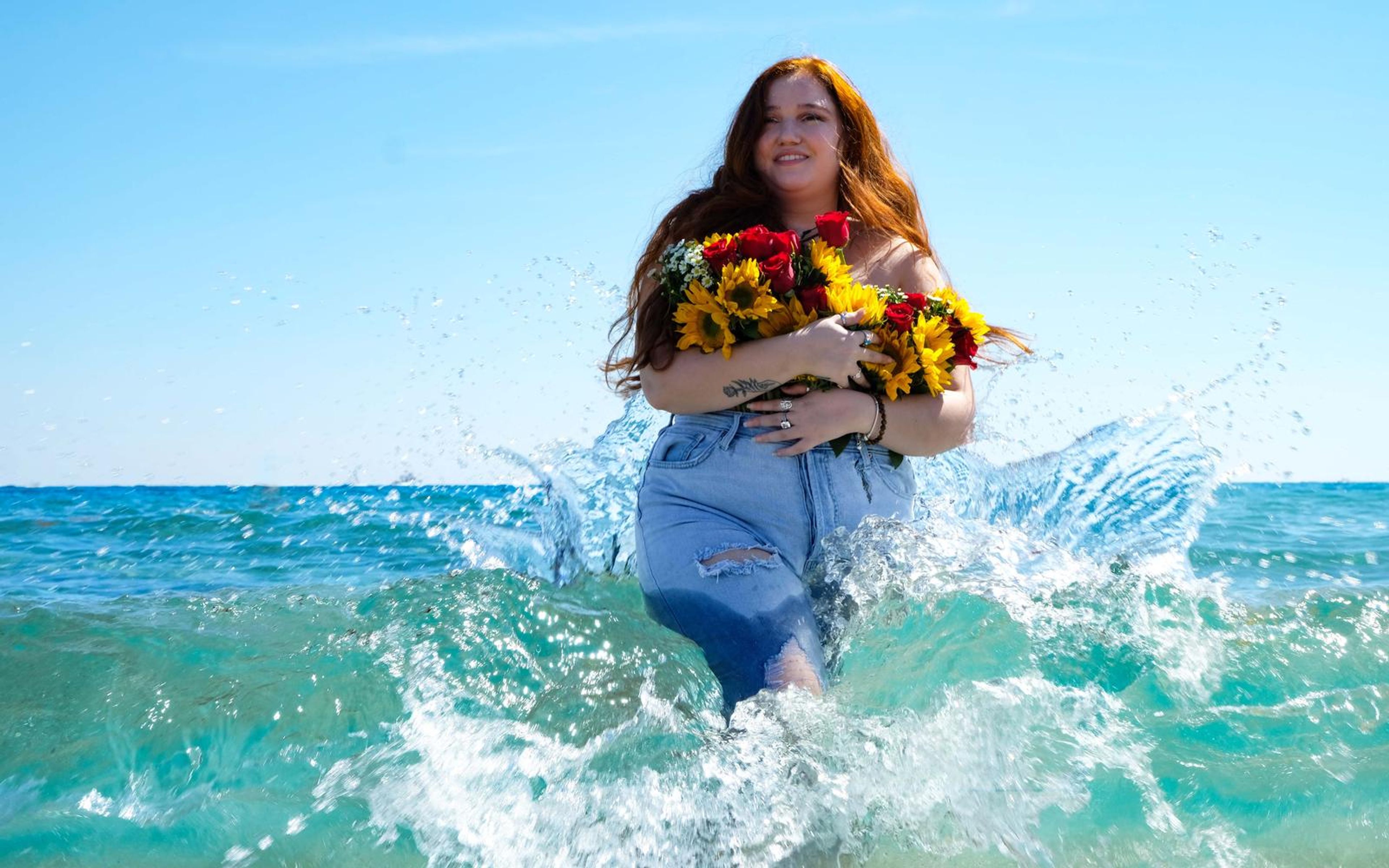 Model wading out through an explosive splash, bouquet held to chest, bright turquoise sea