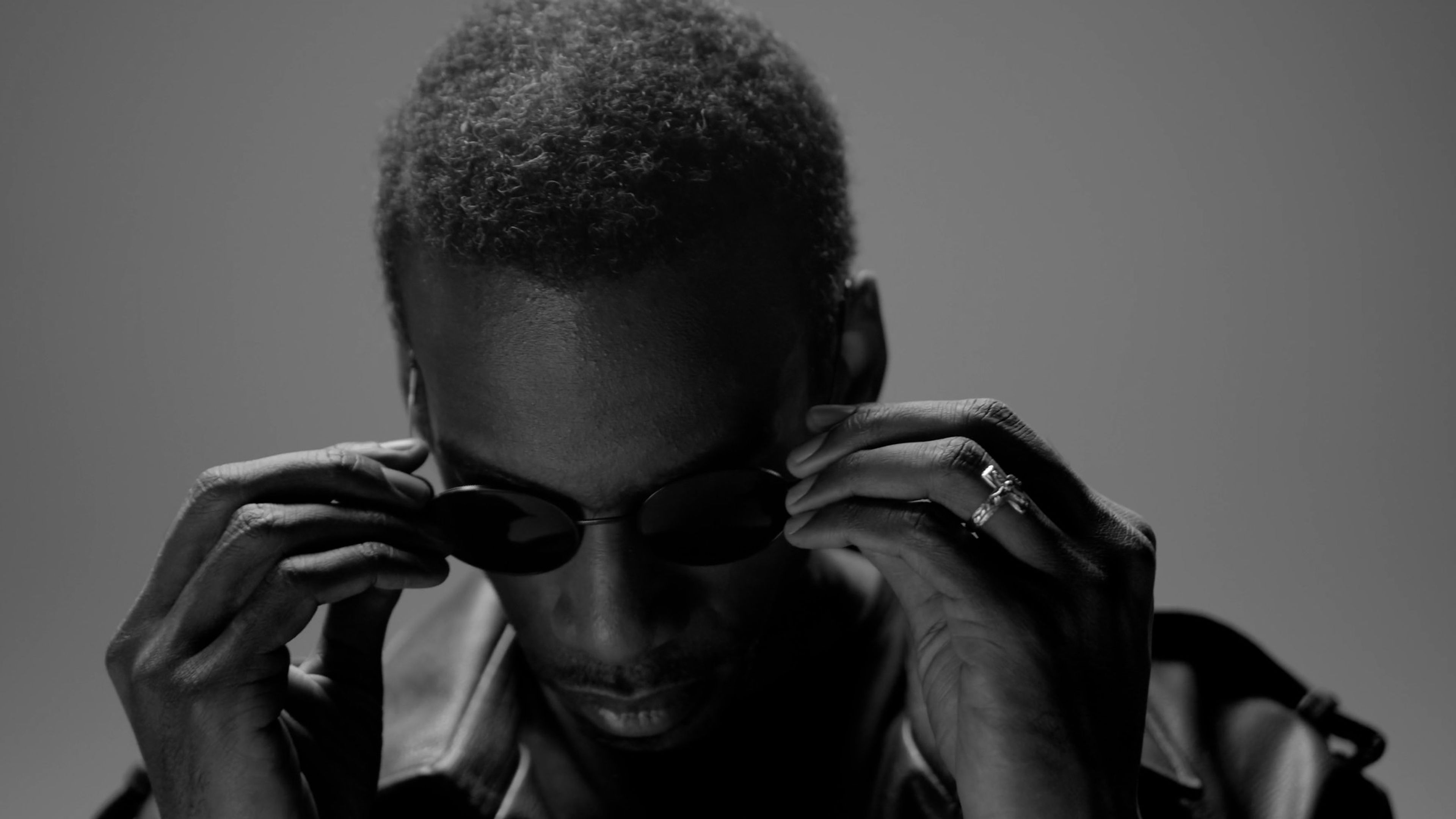 Black-and-white close-up of a man adjusting his sunglasses with both hands