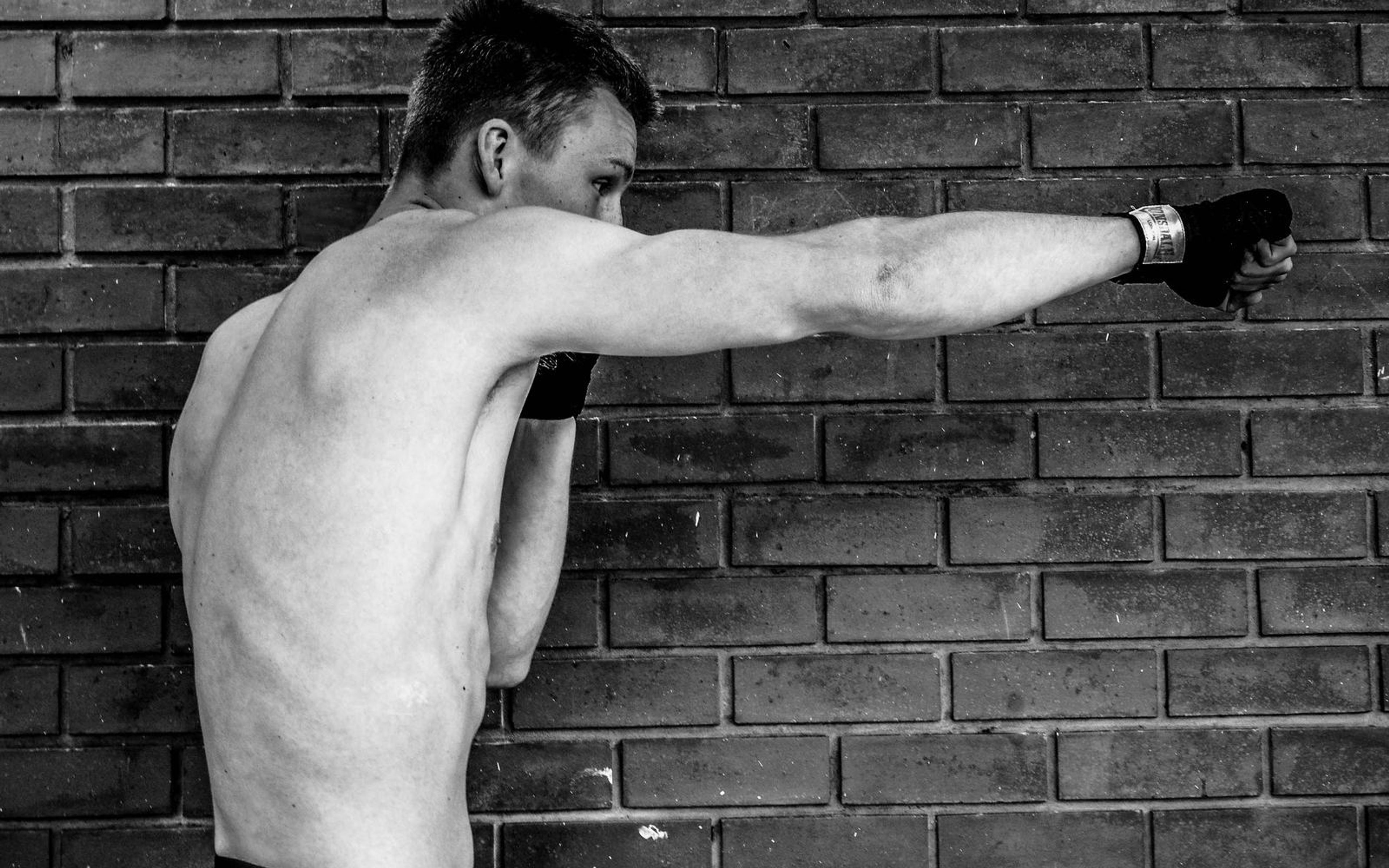 Black and white image of a man throwing a straight punch, arm extended, brick wall behind
