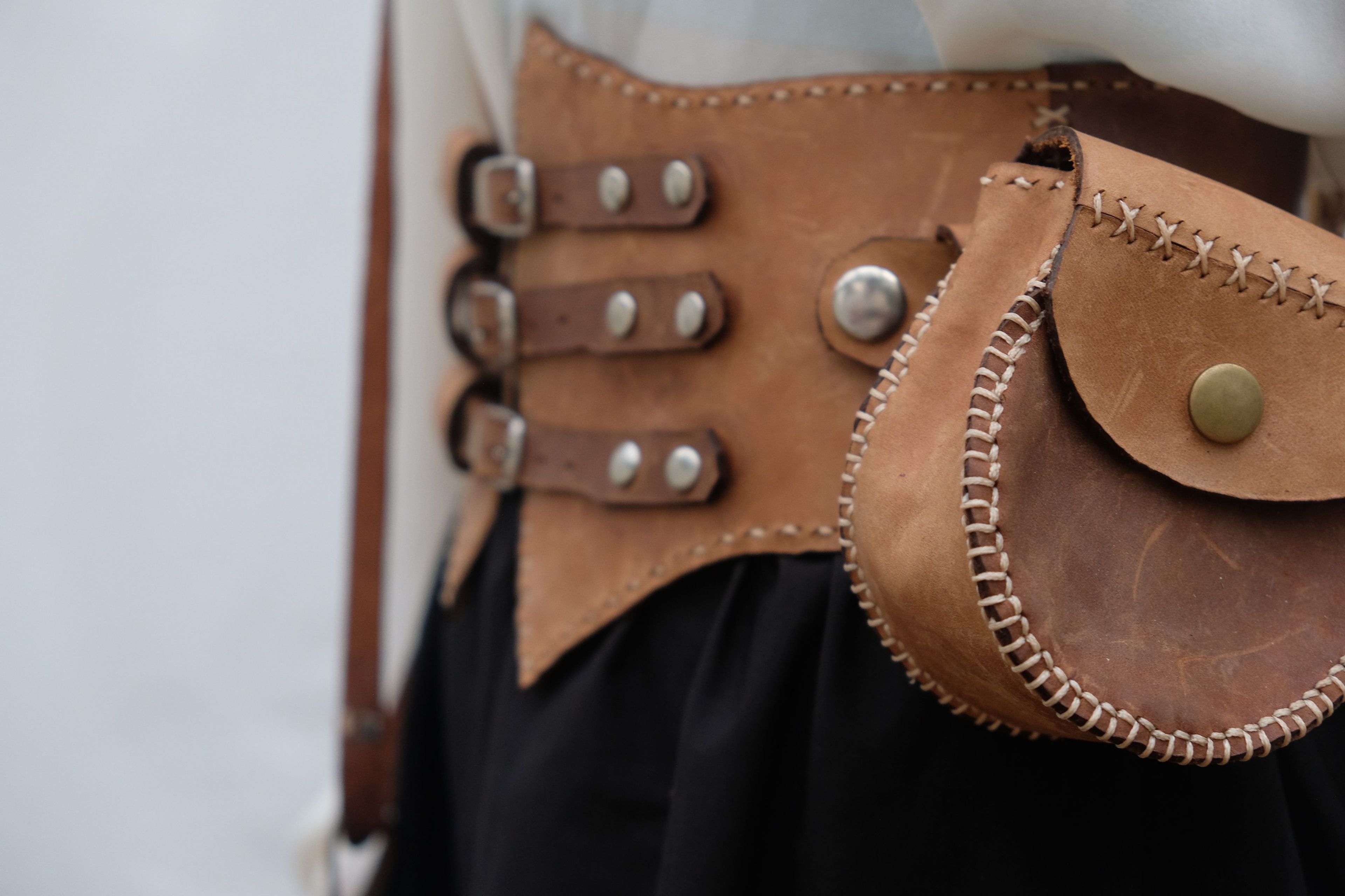 Close view of a tan leather corset belt with buckled straps and a round leather pouch