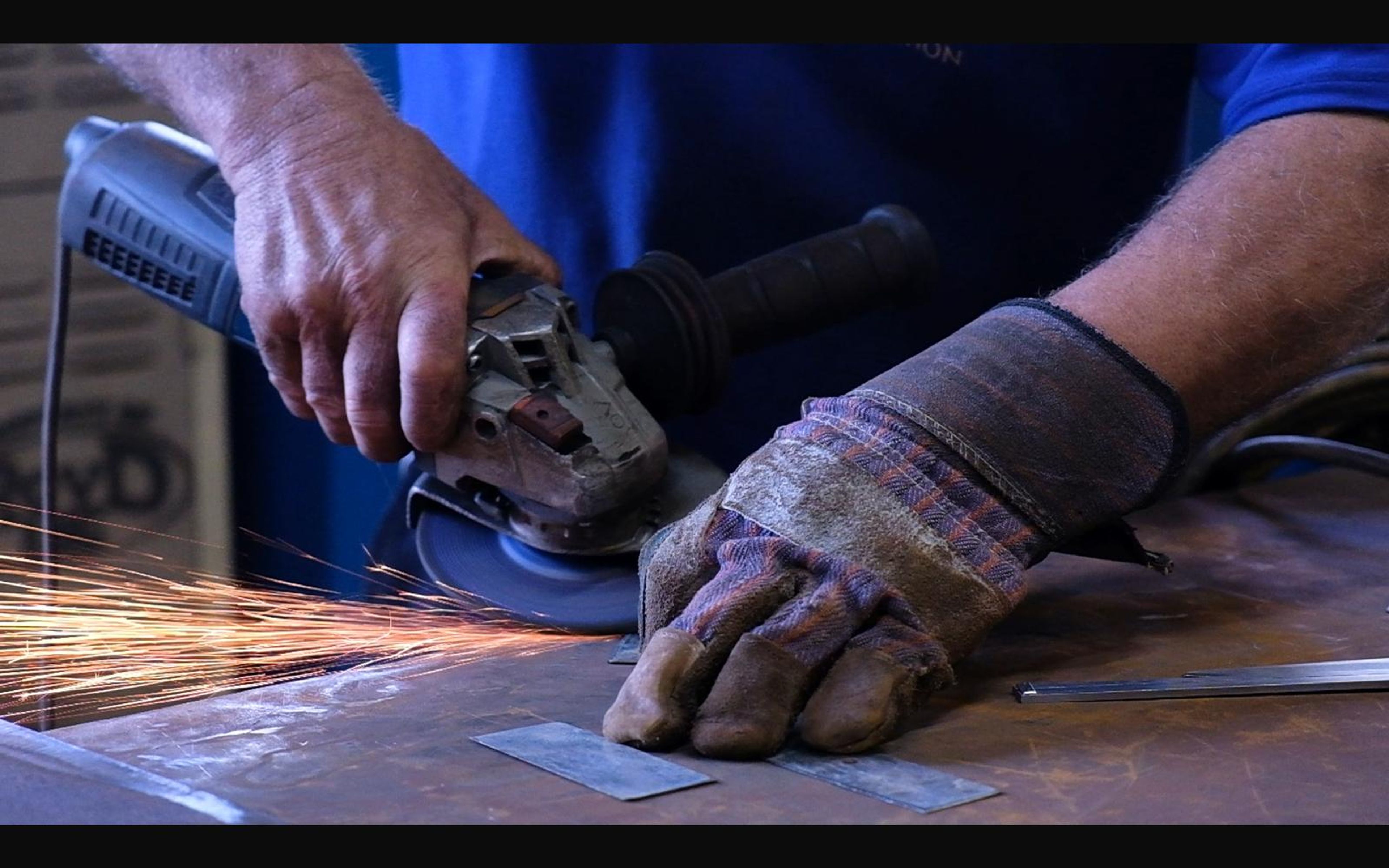 Gloved hands grinding a steel plate