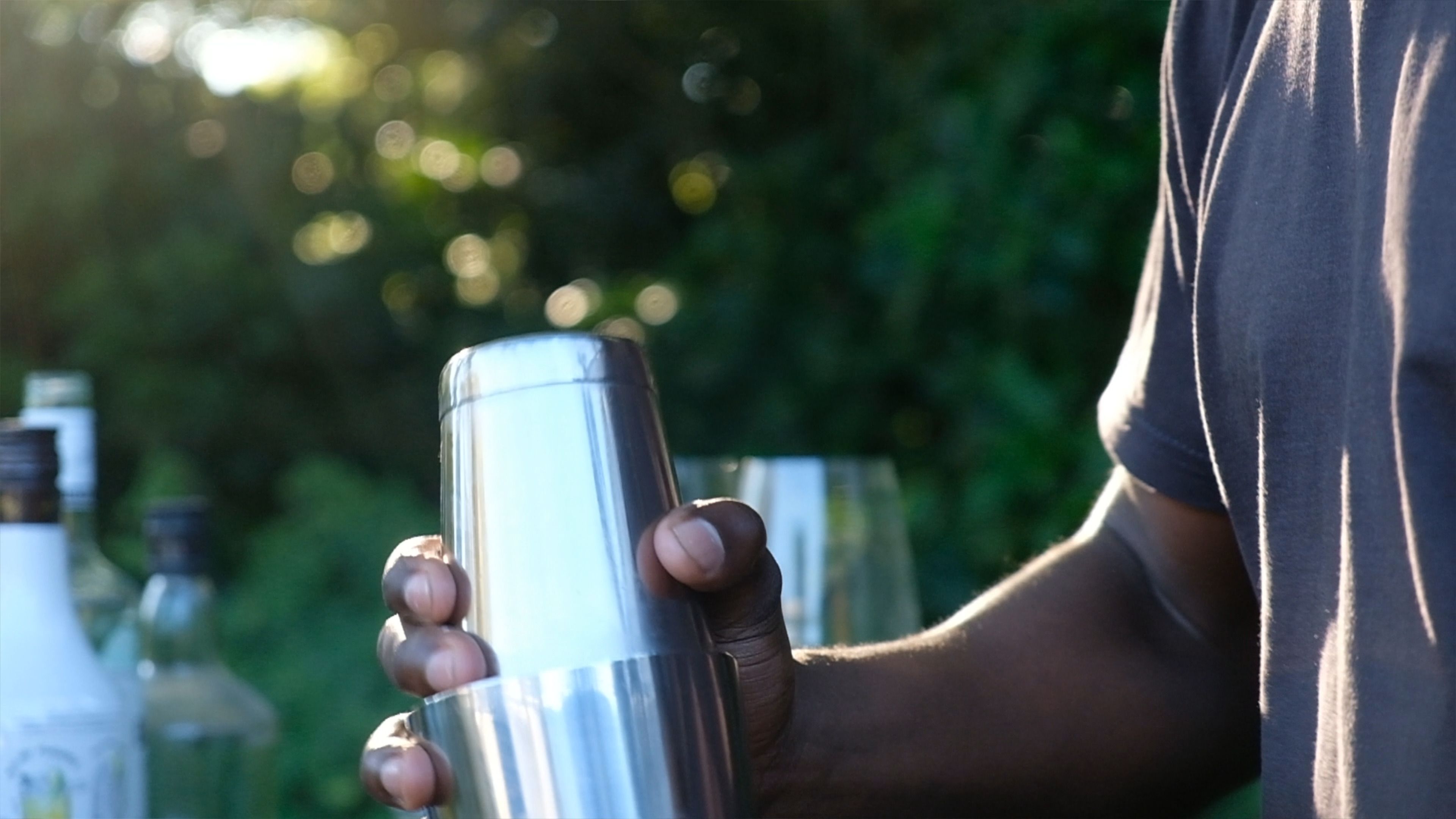 Hands shaking a metal cocktail shaker outdoors