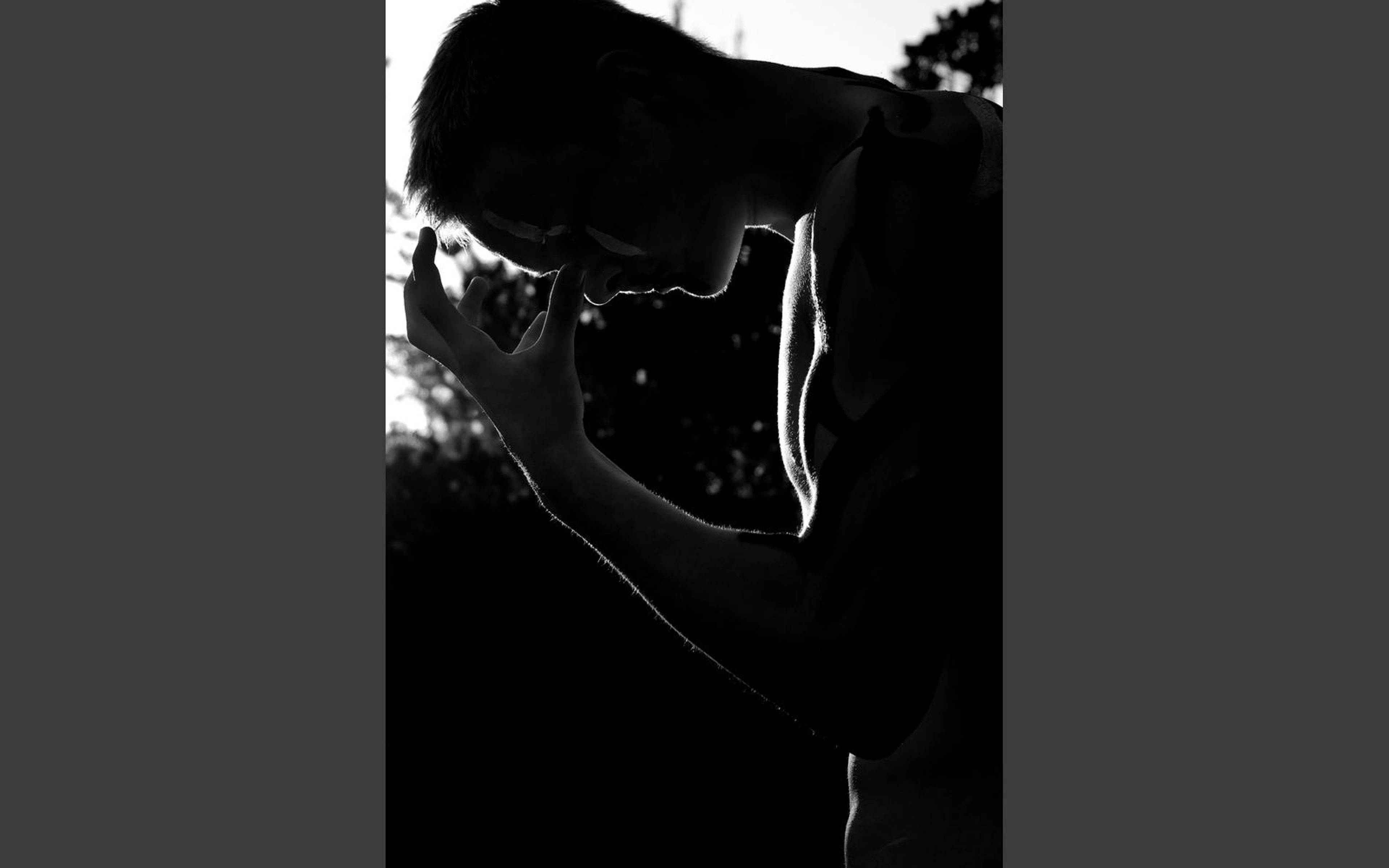 Monochrome silhouette of the performer with a hand to his face against dark branches