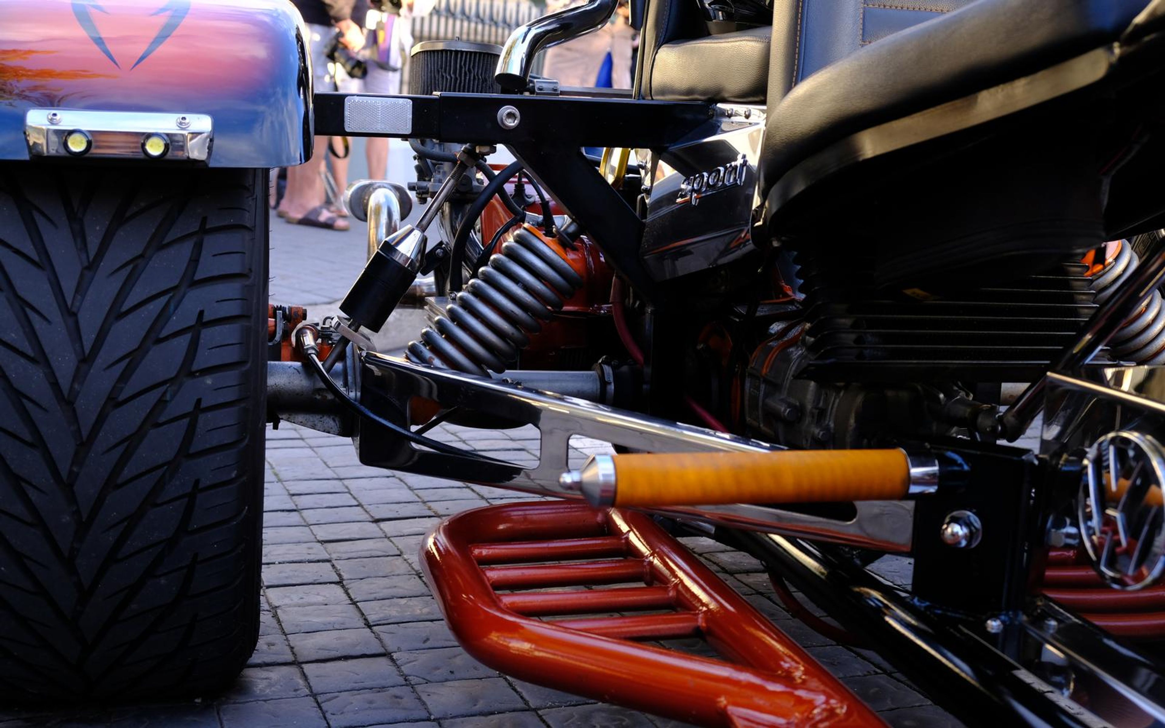 Wide treaded rear tyre, orange footboard and engine detail of a trike, shot close to the ground