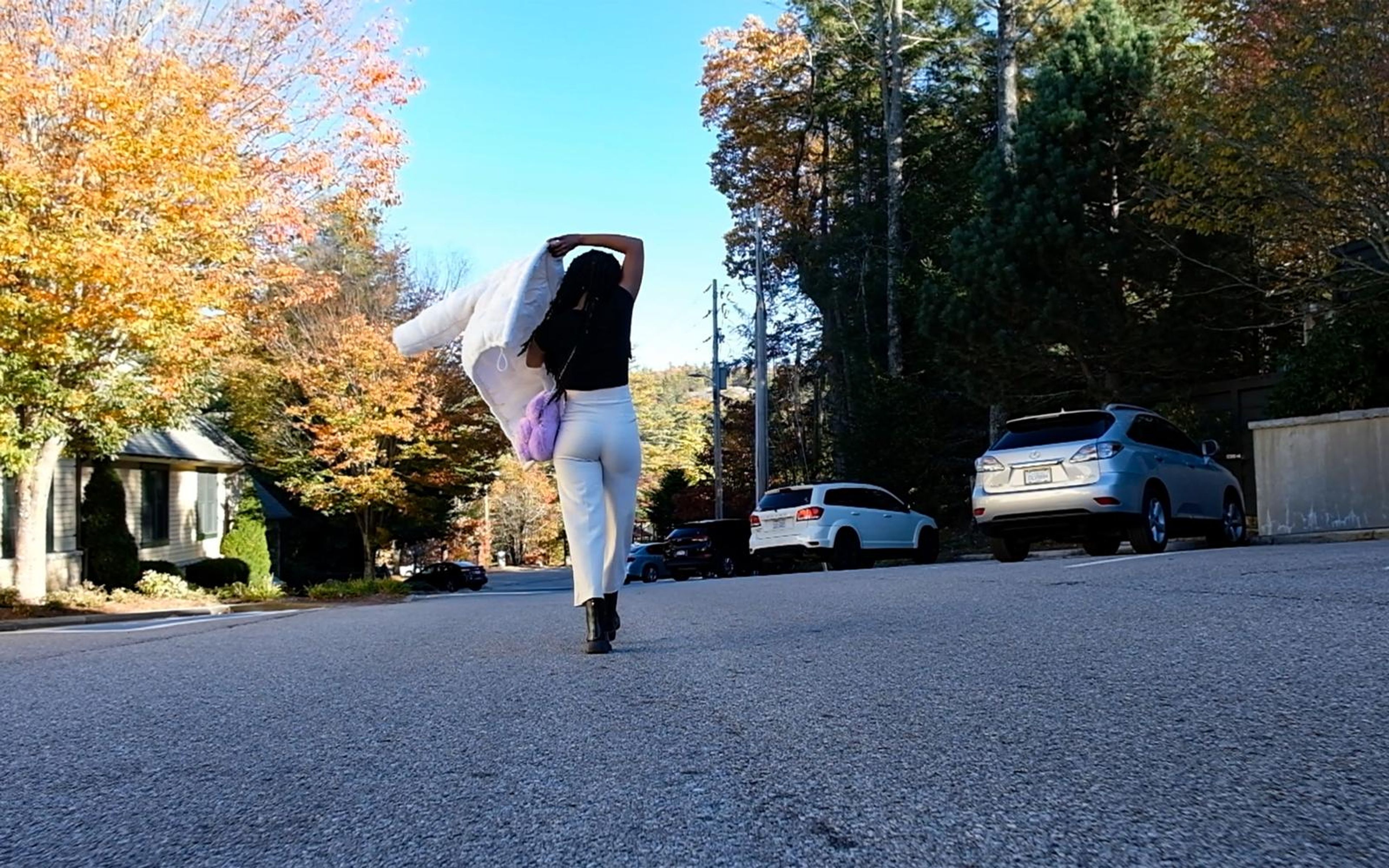 Model walking away down the road with the jacket over her shoulder, autumn trees and parked cars