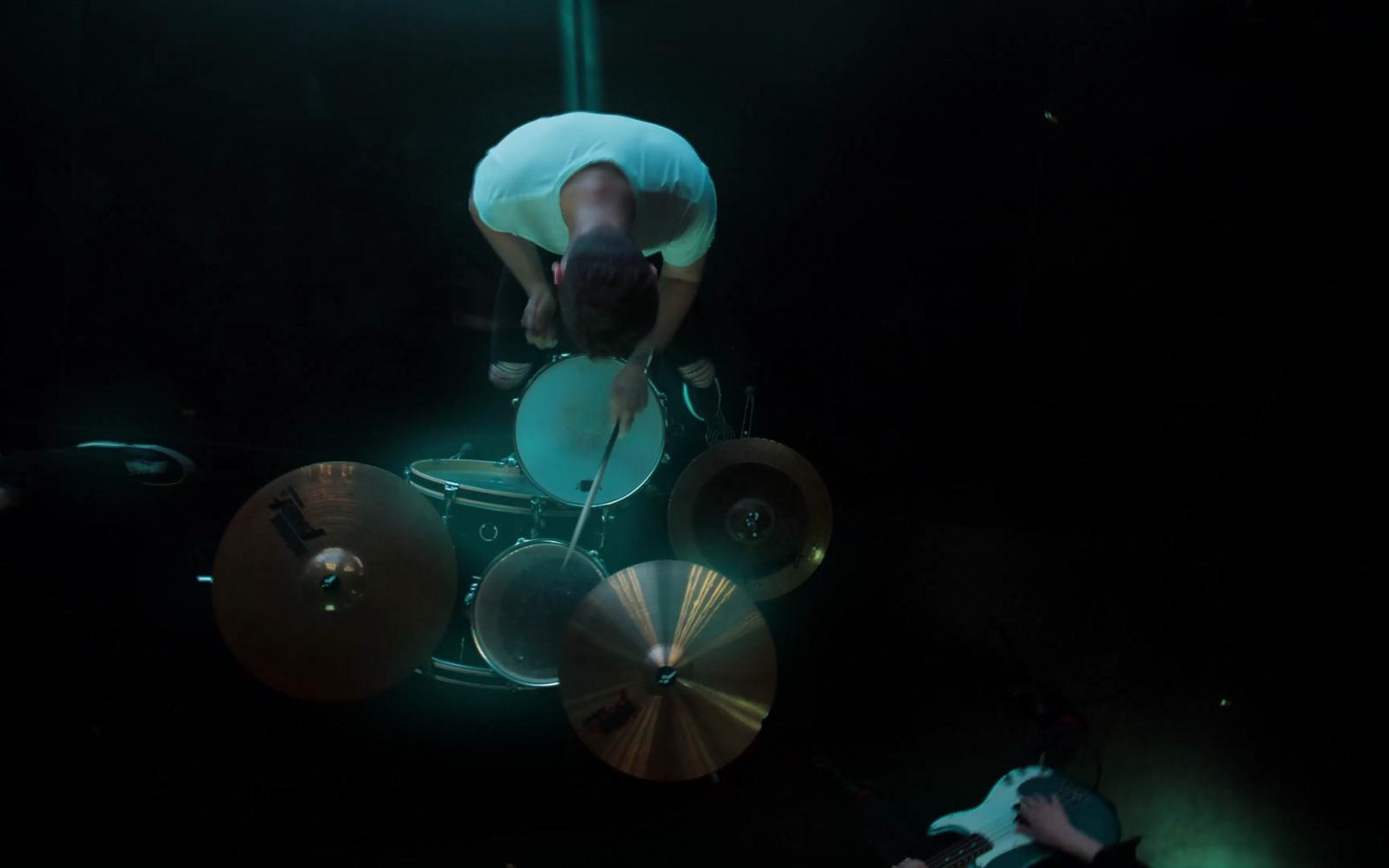Overhead view of a drummer at a kit with cymbals glowing teal in the dark
