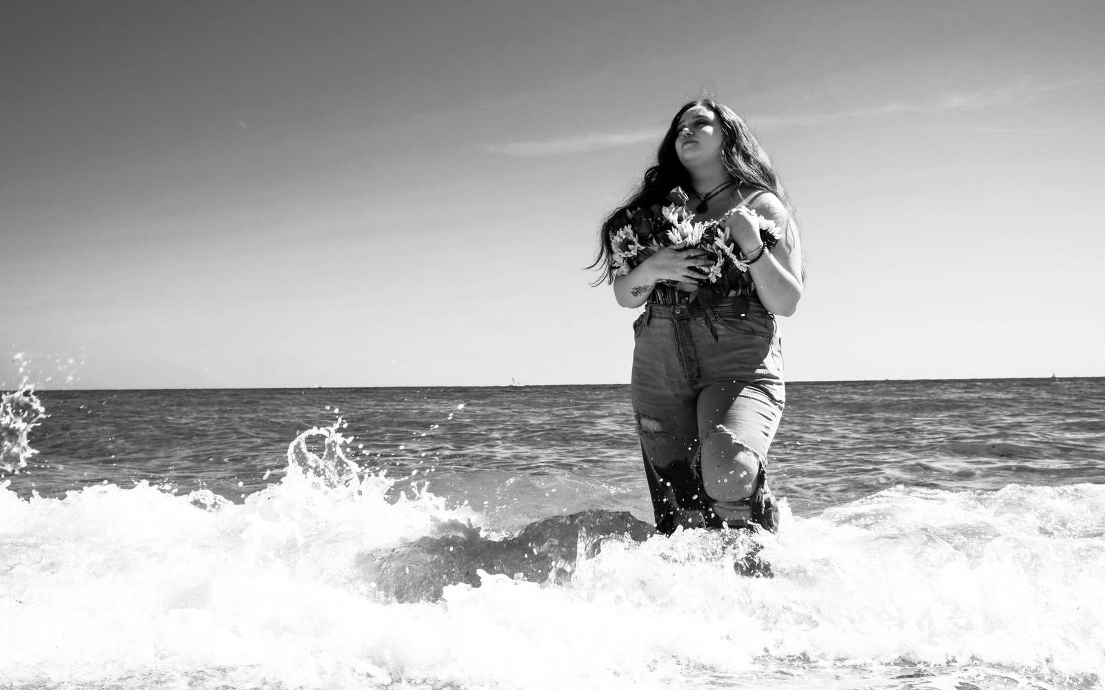 Black and white frame of model looking up in shallow sea, a wave splashing at the left edge