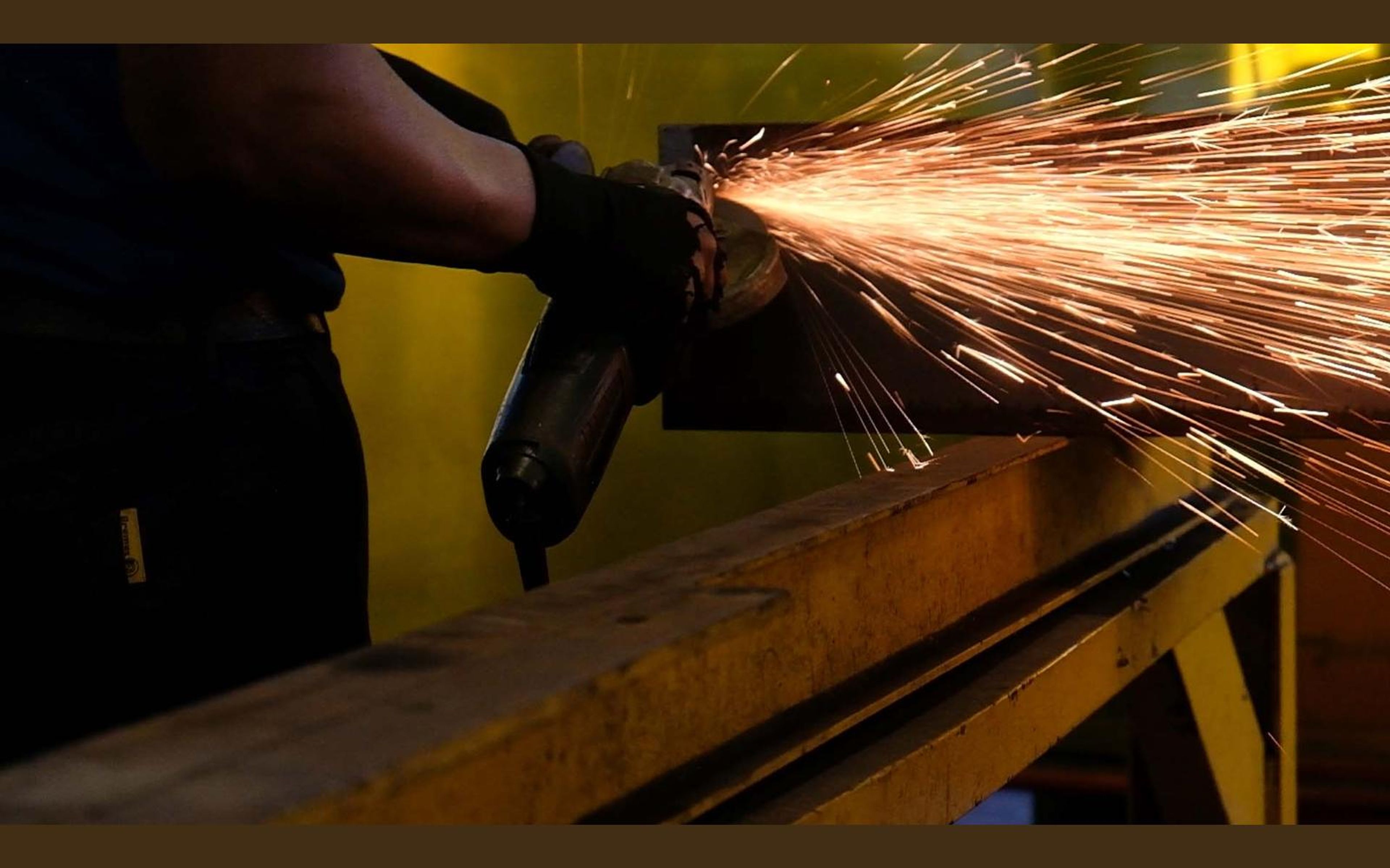 Gloved hands grinding a steel plate