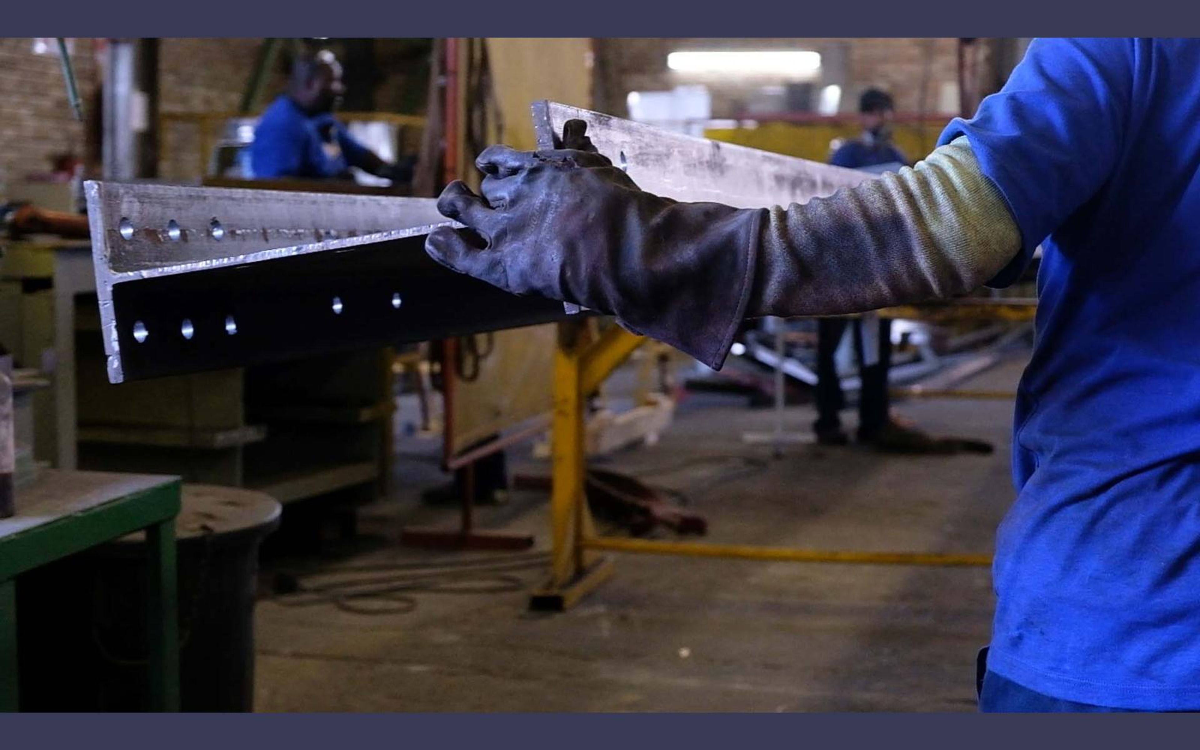 Fabricators at work among steel beams in the shop