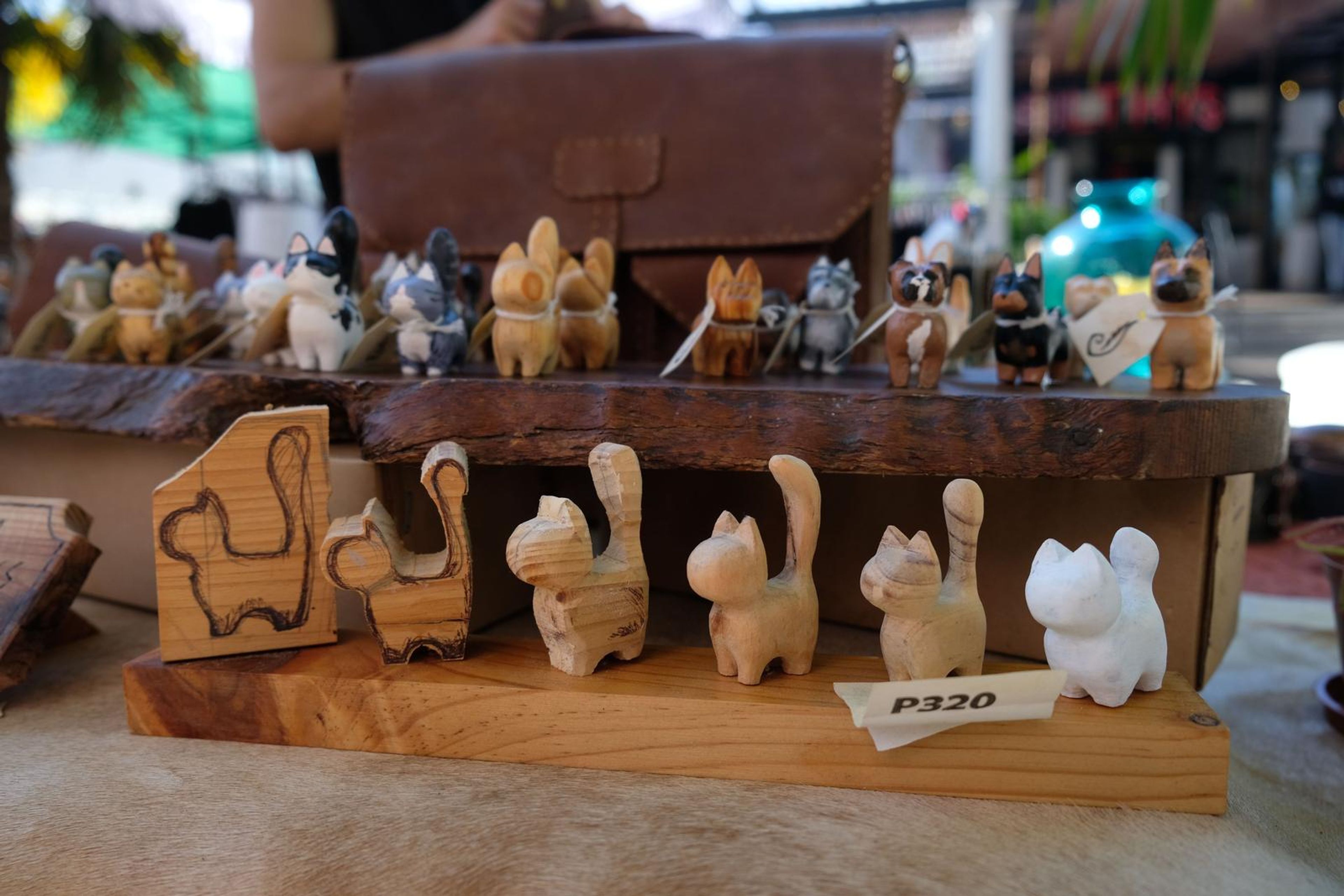 Hand-carved wooden cats on a bark shelf beside a leather satchel