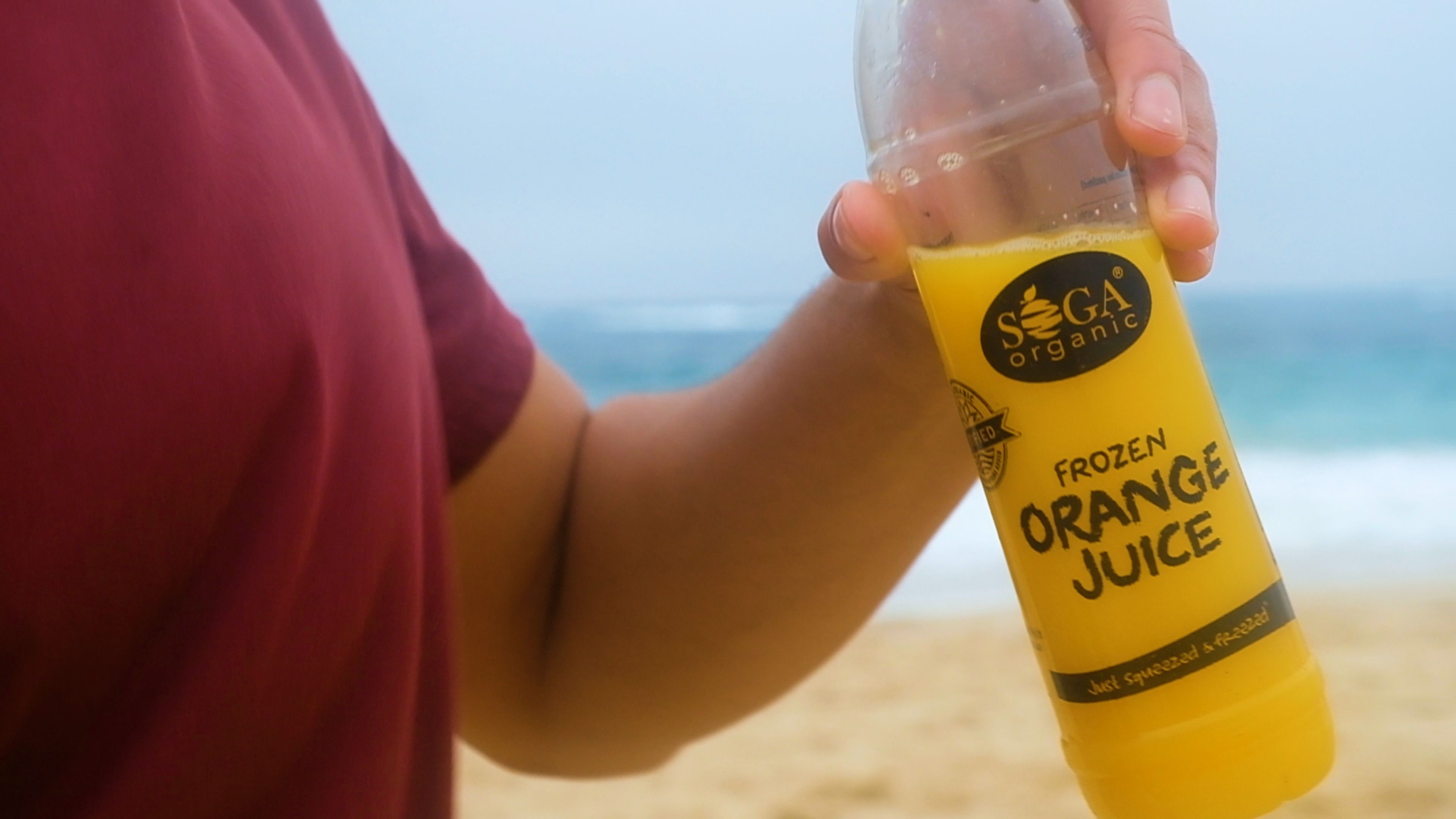 Person holding a bottle of SOGA frozen orange juice on the beach