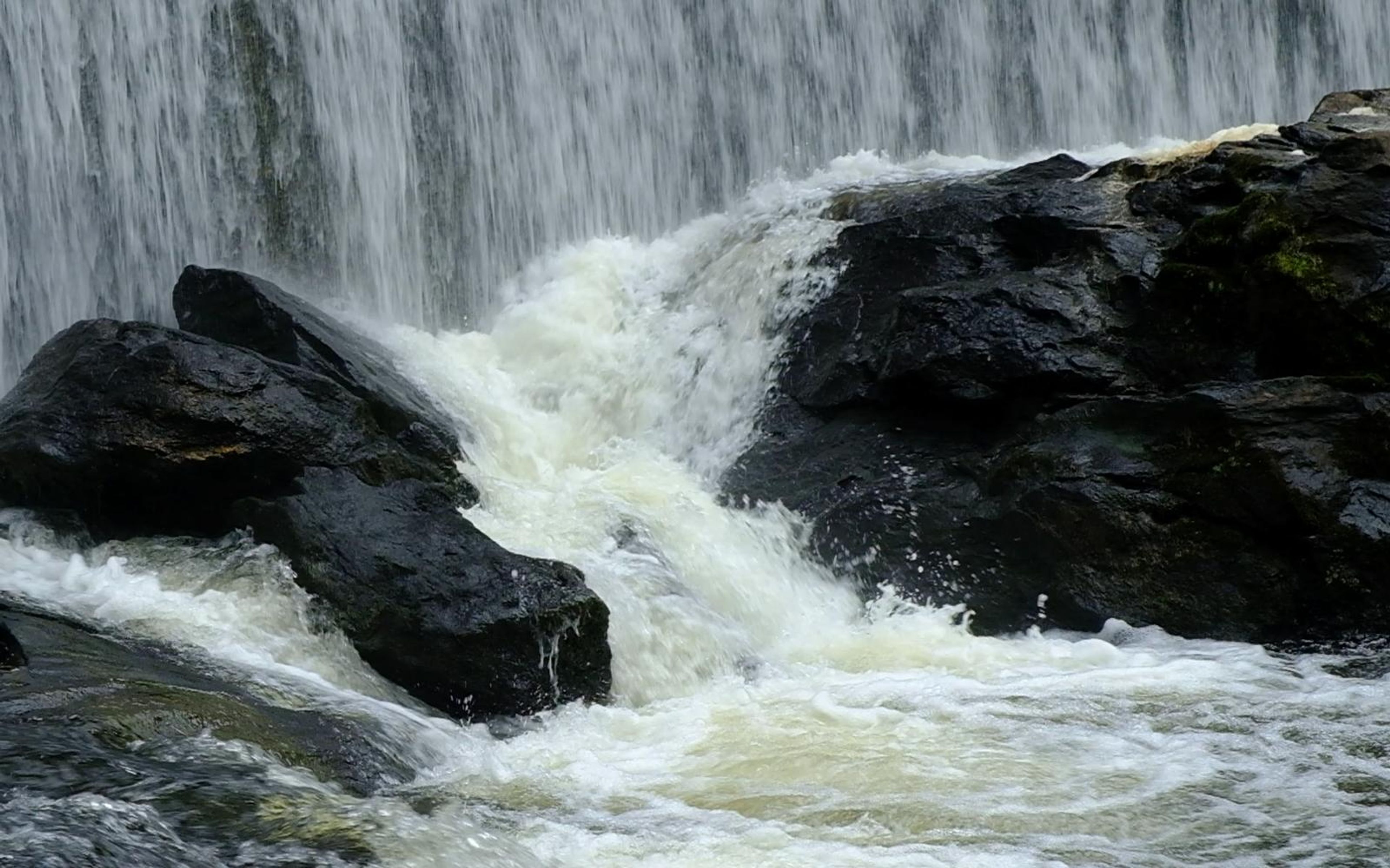 Black boulders splitting the foaming water at the foot of the falls