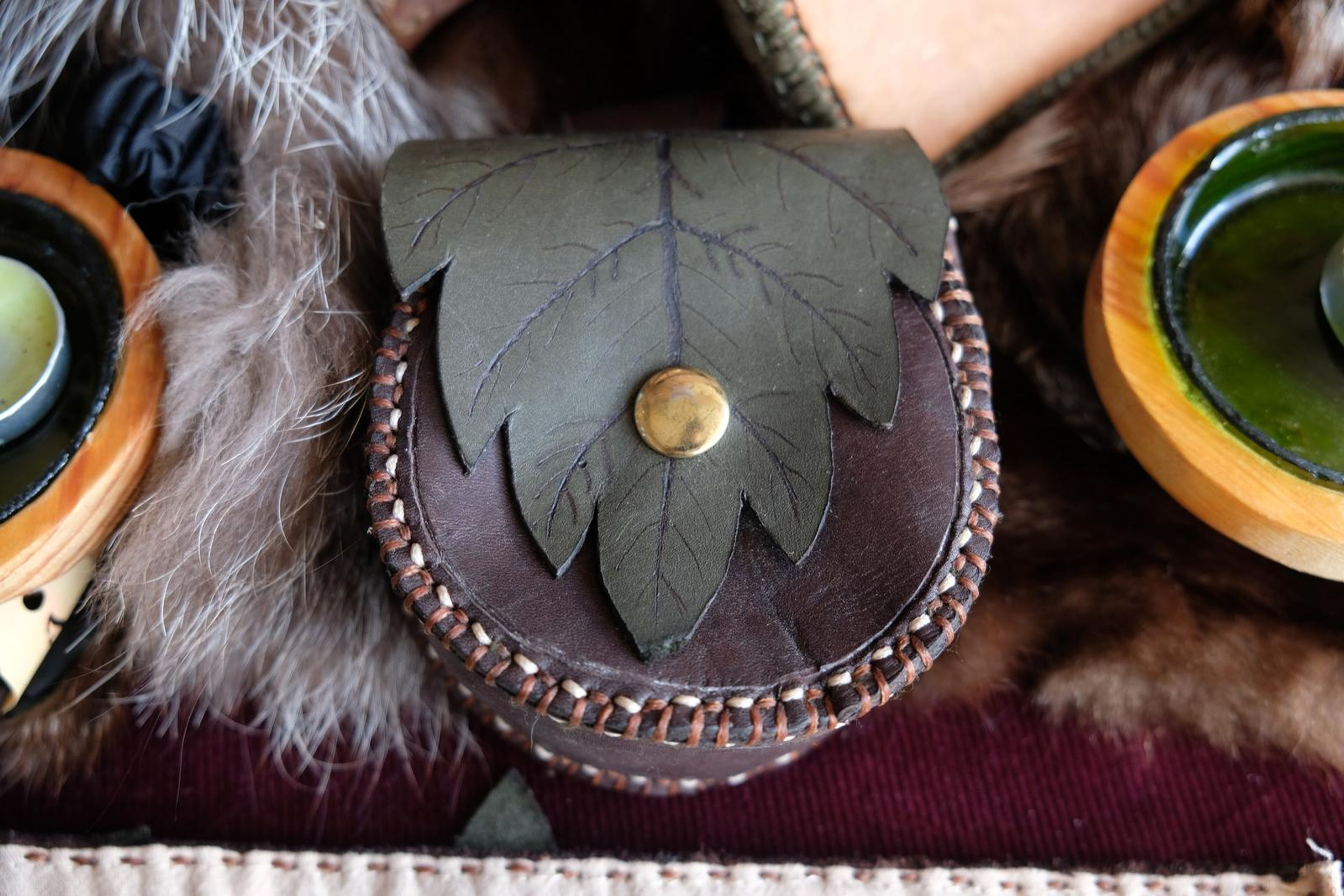 Green leaf-shaped leather pouch with a brass button sitting on fur