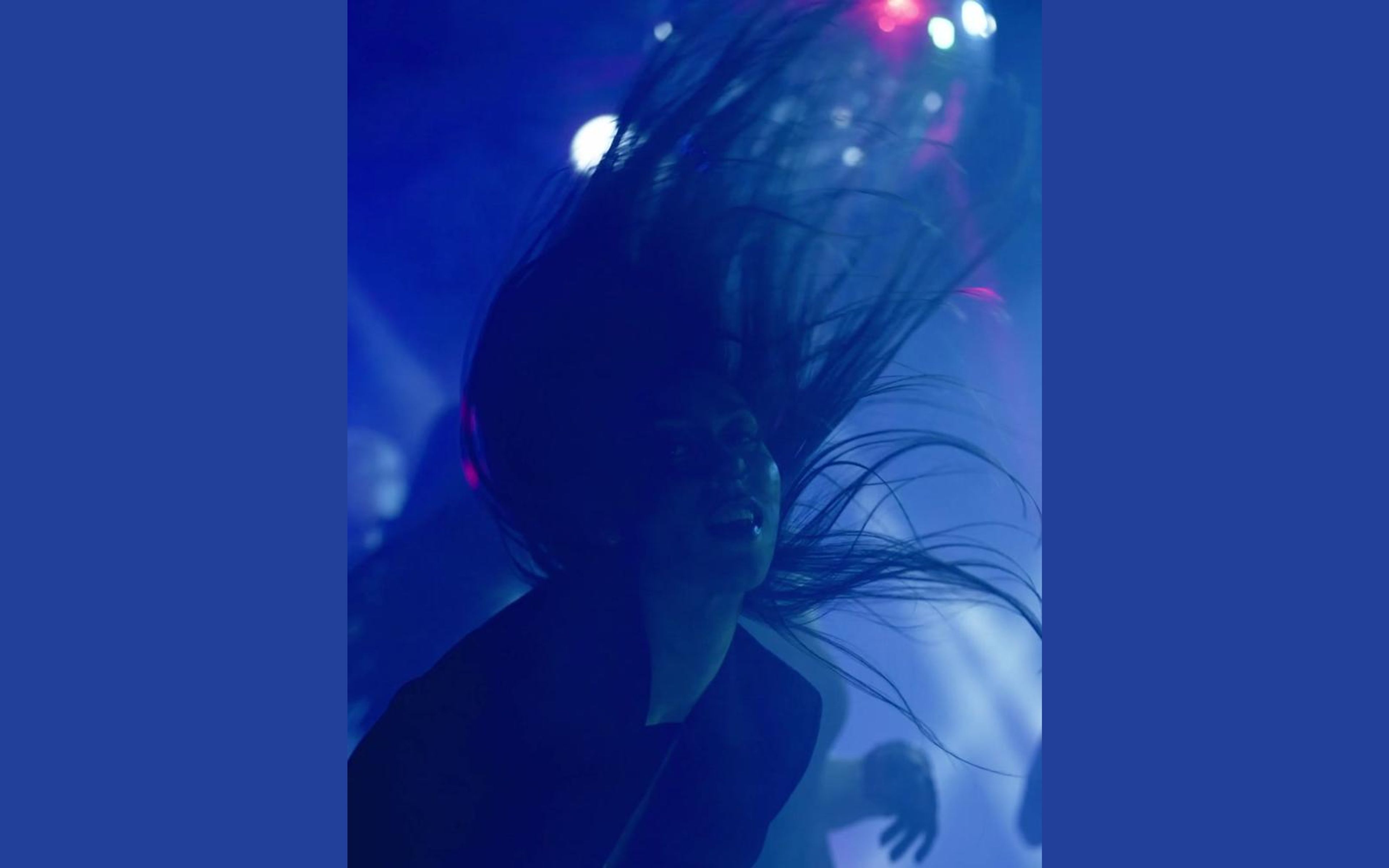 Dancer whipping long dark hair through blue stage light with bright bokeh highlights