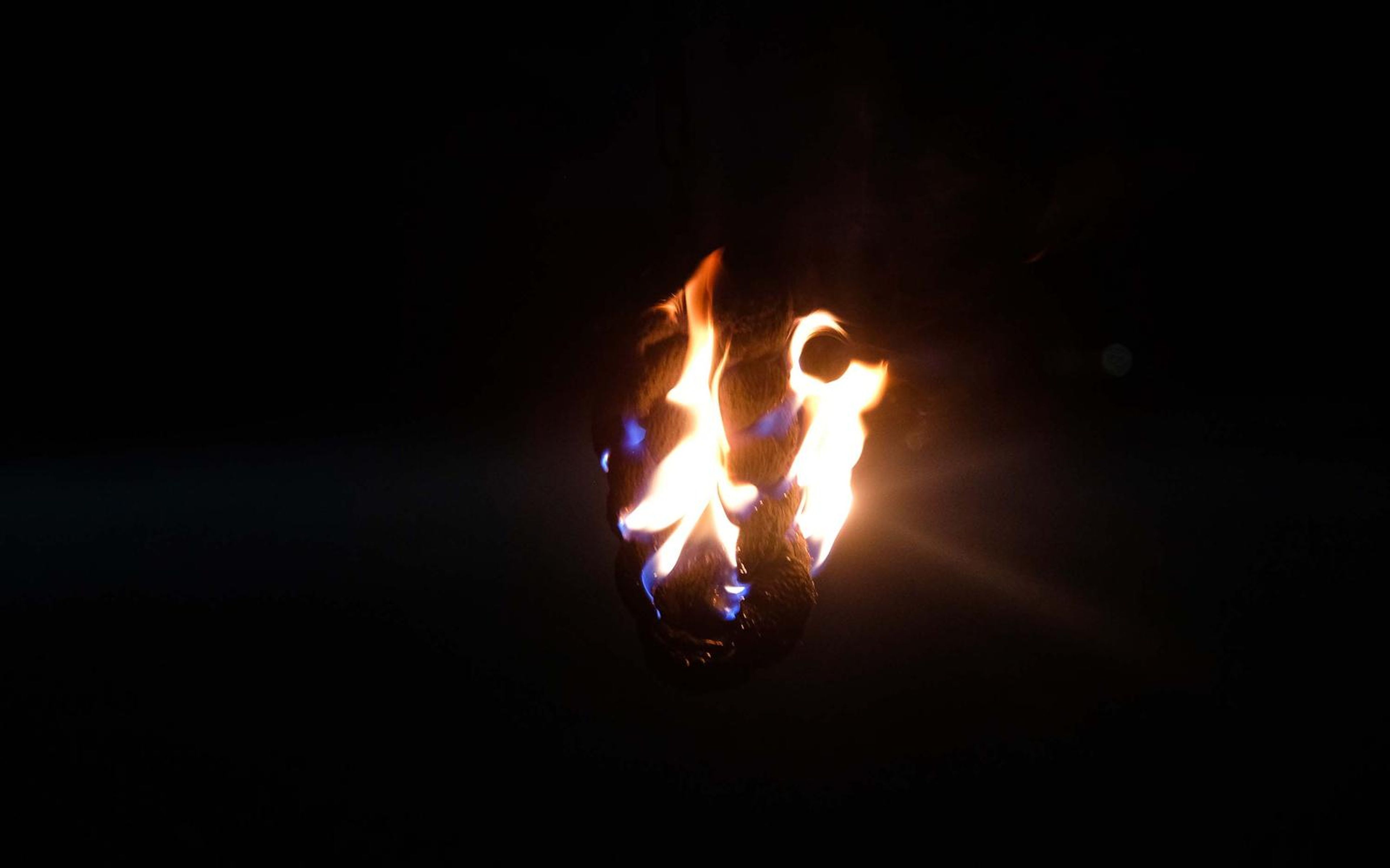 Fire ball hanging in darkness with blue-edged flames and a soft light flare