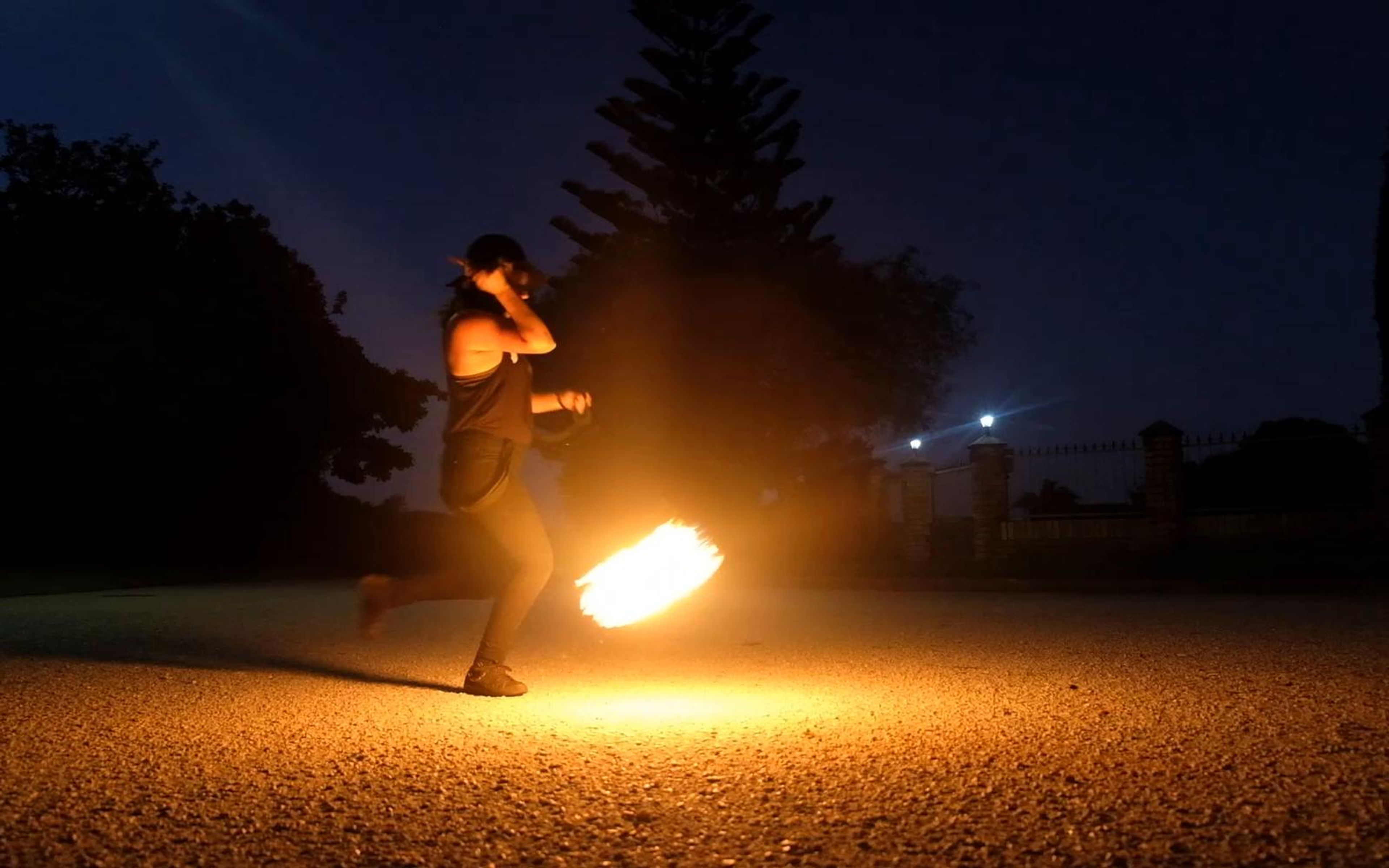 Performer walking with a flaming torch in an open lot at dusk