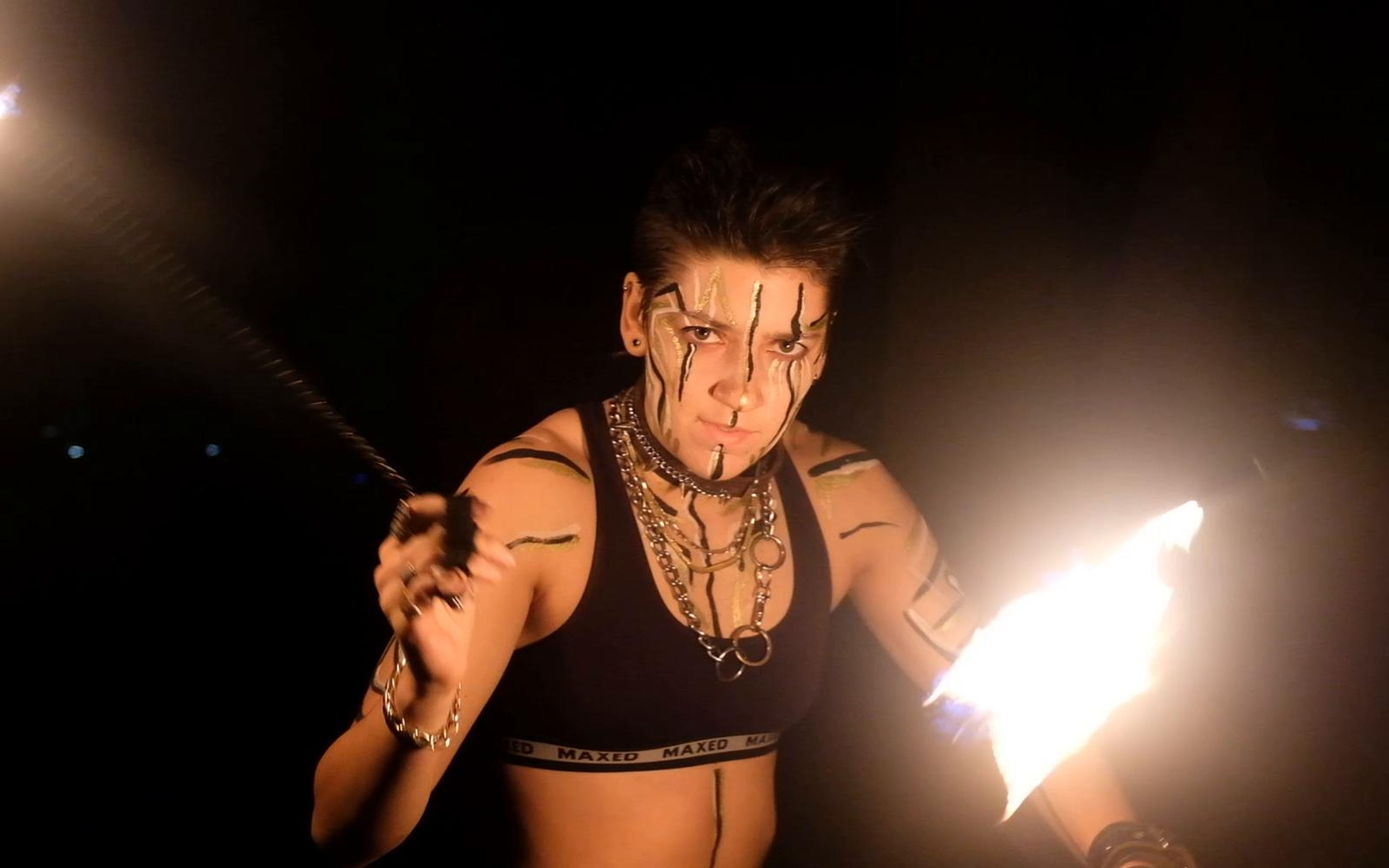Performer with a painted face and a staff glowing with fire in front of a dark backdrop