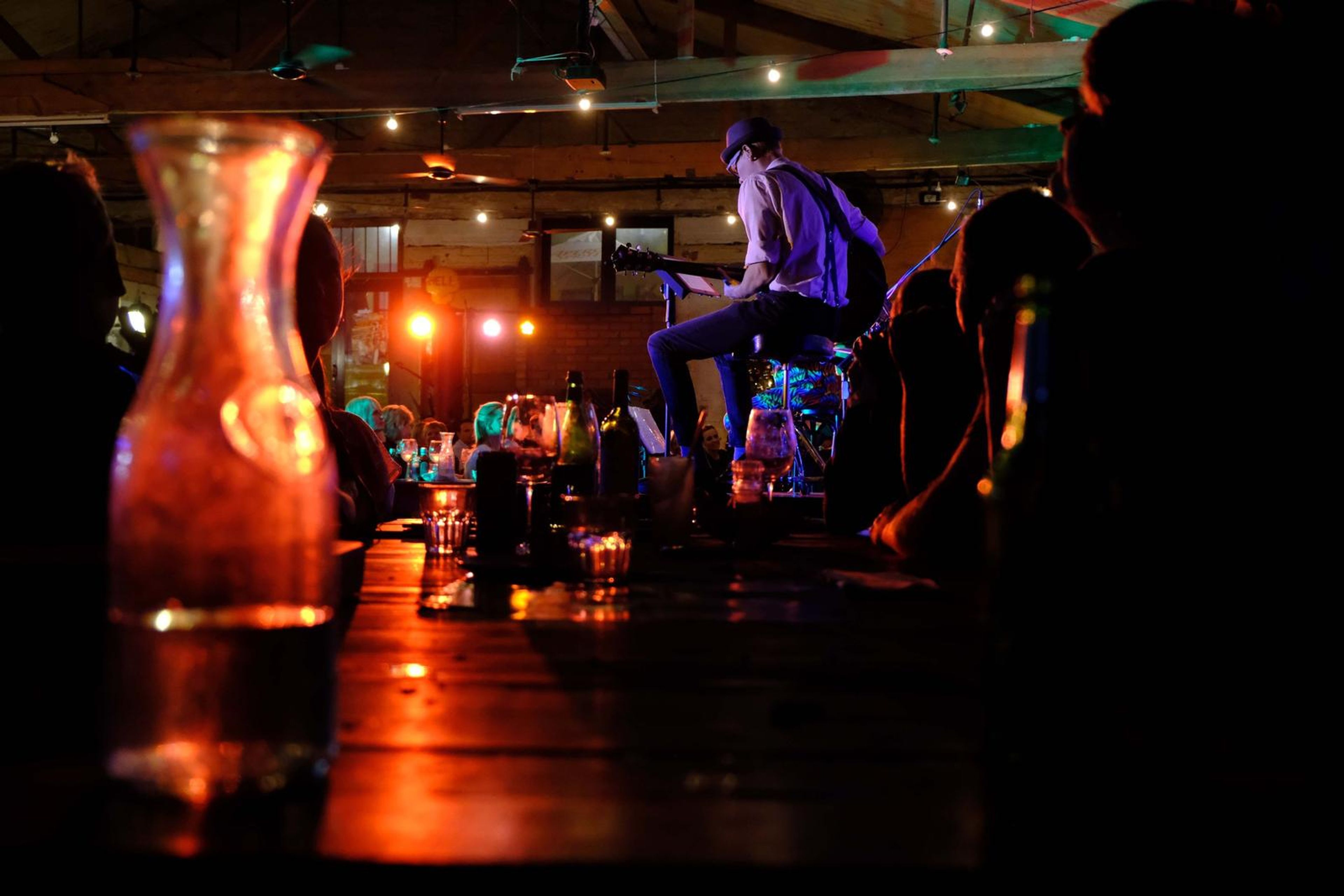 Glass carafe glowing orange on a table with the band behind it