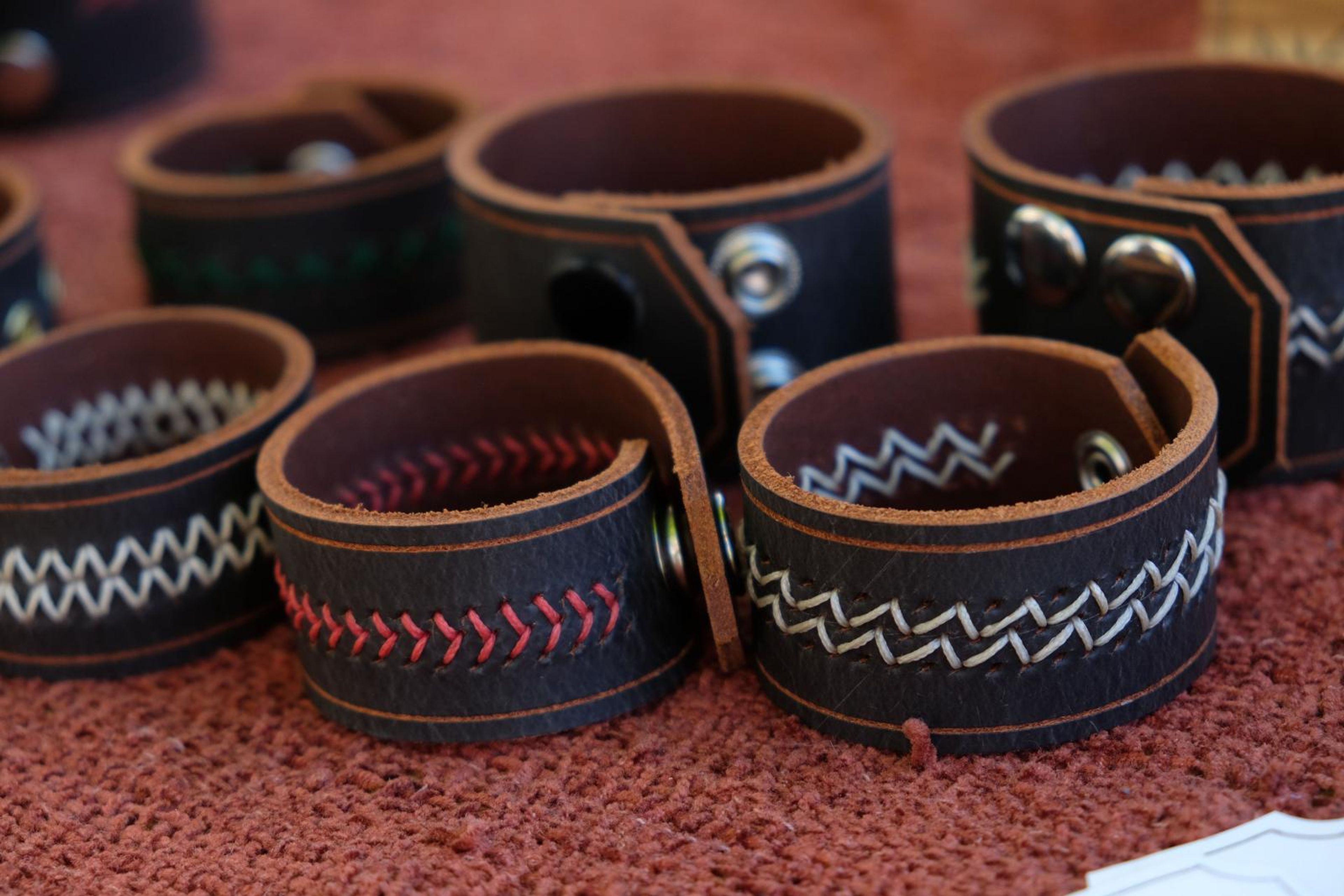 Dark leather cuffs with white and red stitching on red cloth