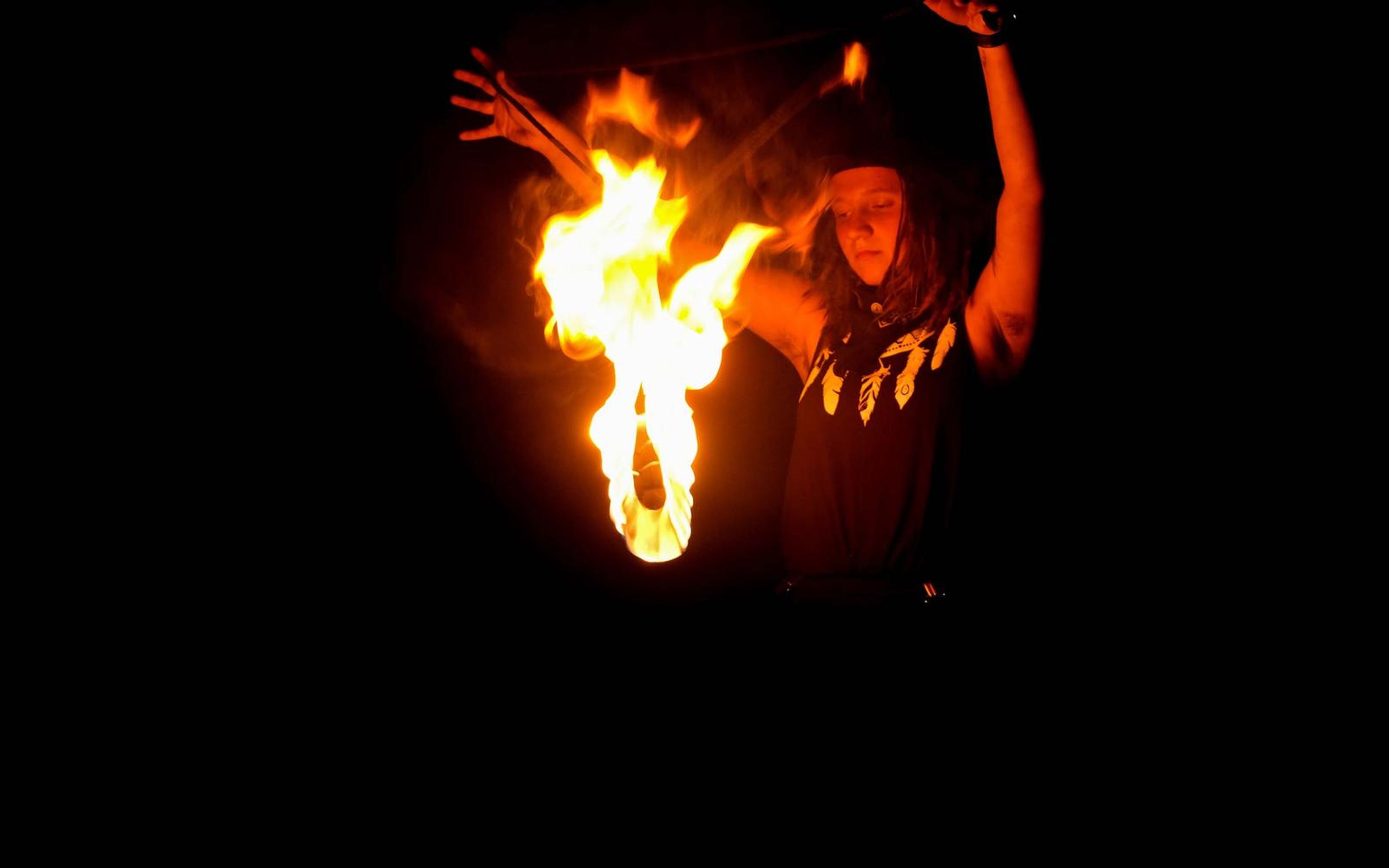 Flame lifted high beside the performer's head, arms raised, dark background