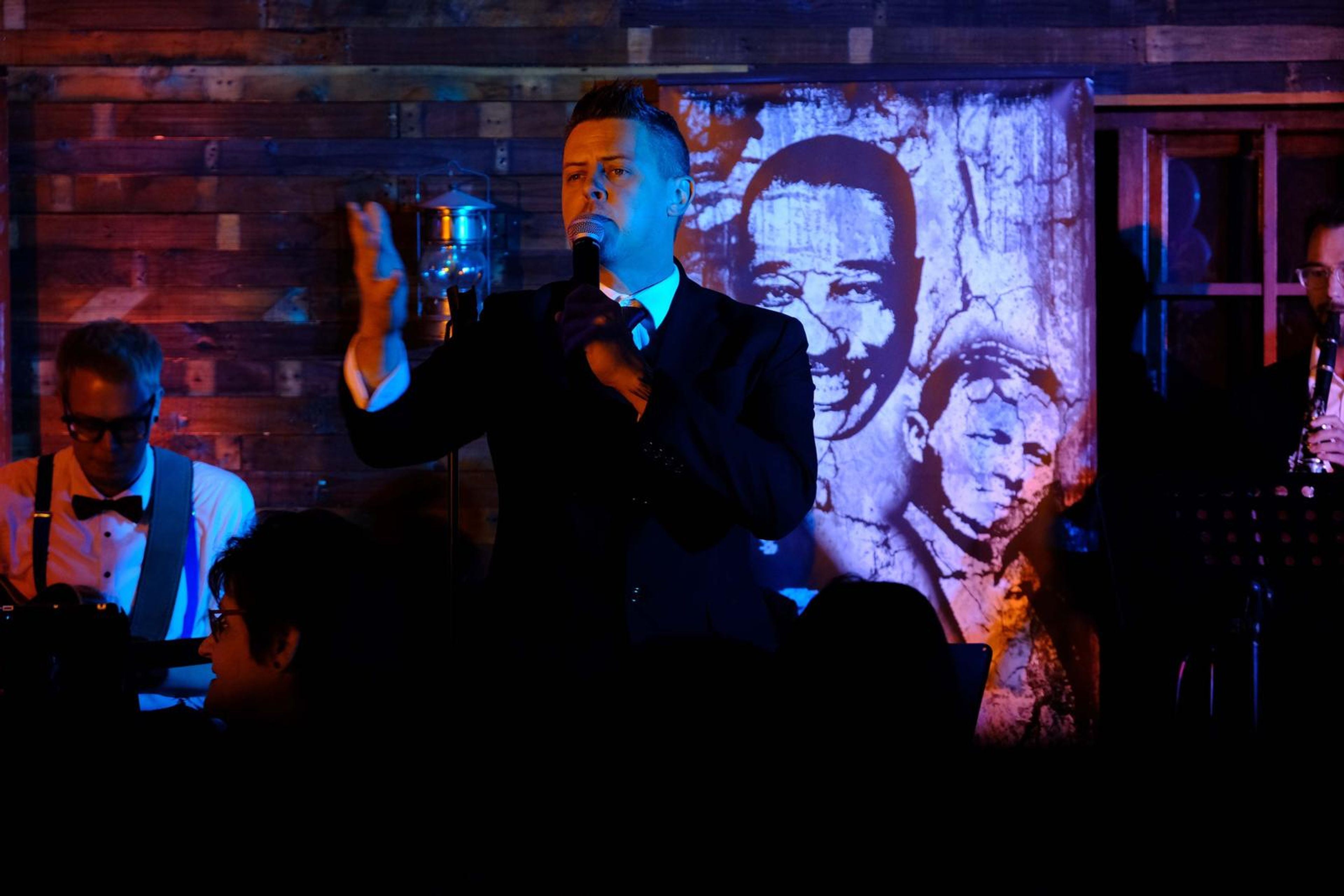 Singer in a suit gesturing to the crowd in front of a jazz mural
