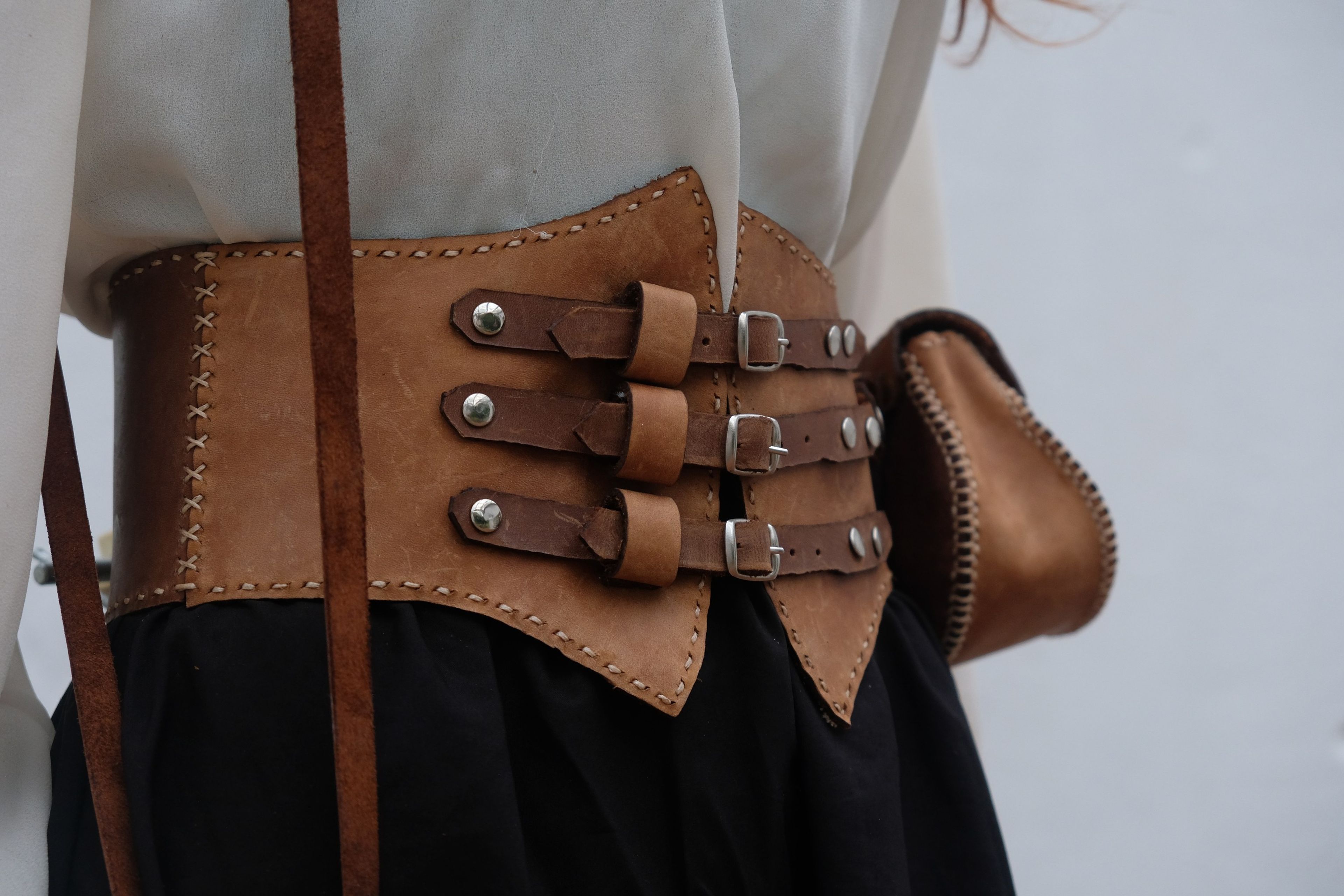 Close view of a leather corset belt with three buckled straps and a small pouch over a black skirt