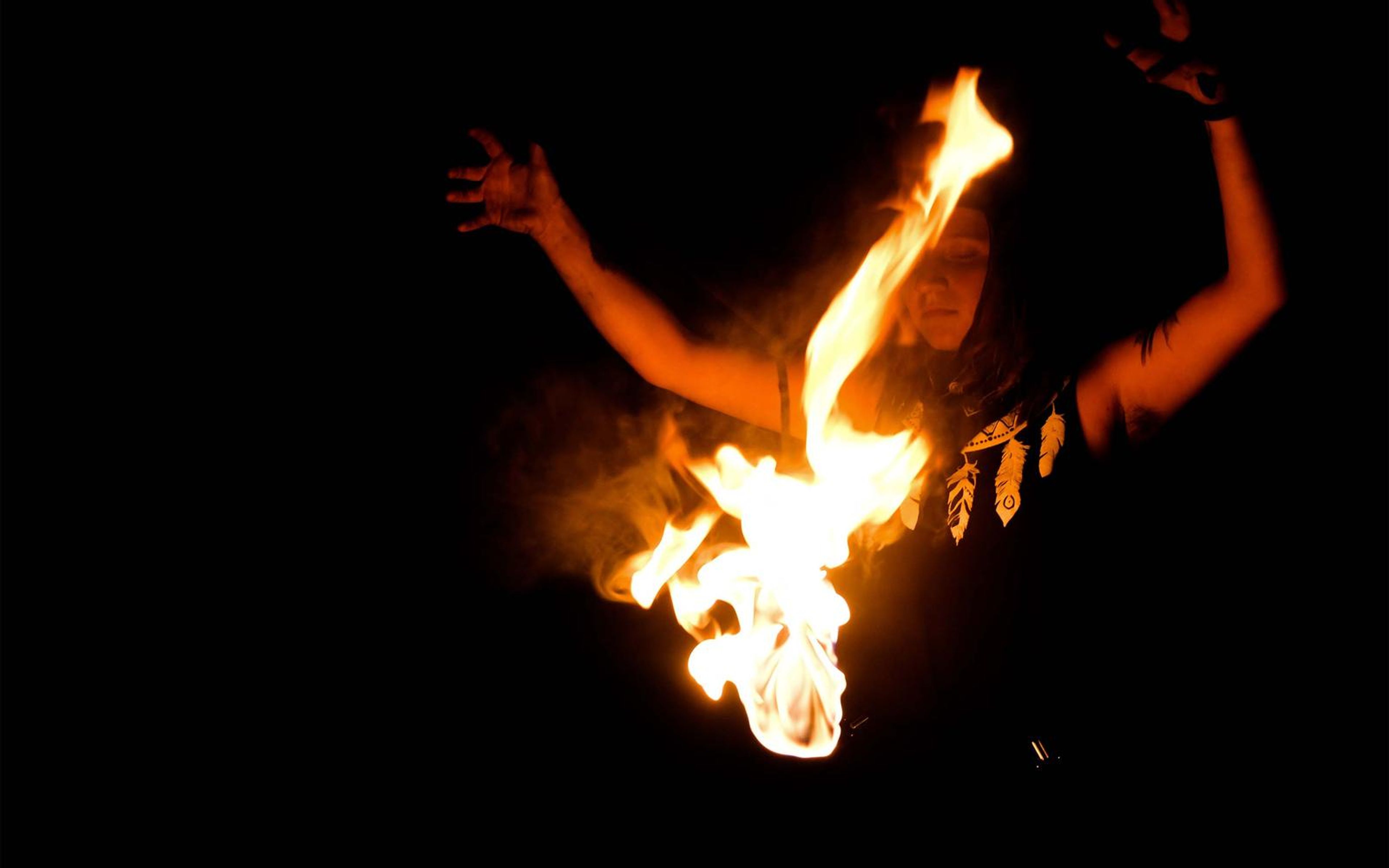 Tall flame rising diagonally from a prop at the chest as the performer raises both arms