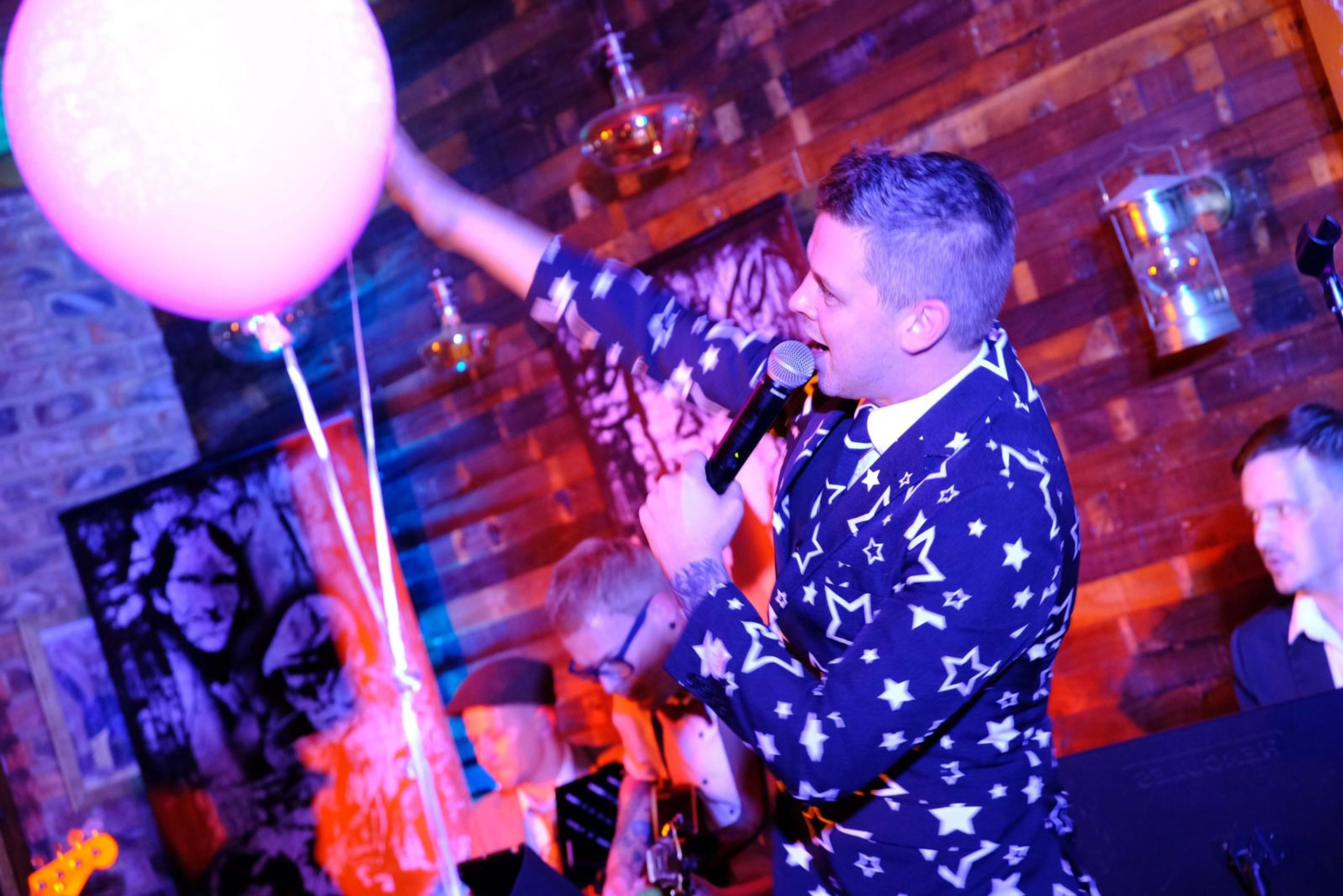 Singer in a star-patterned suit with a pink balloon, mid-song