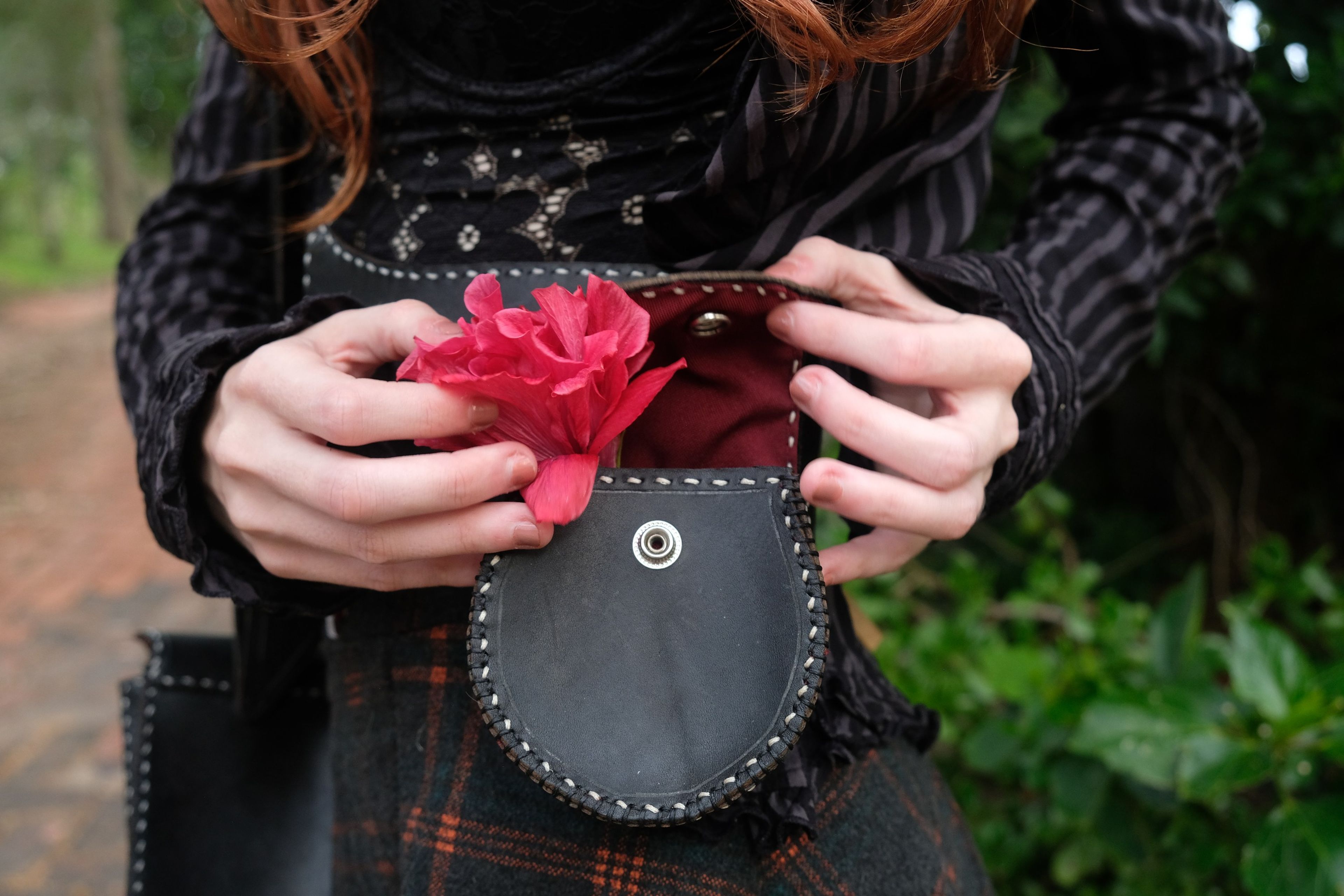 Hands holding a red flower inside a black leather pouch