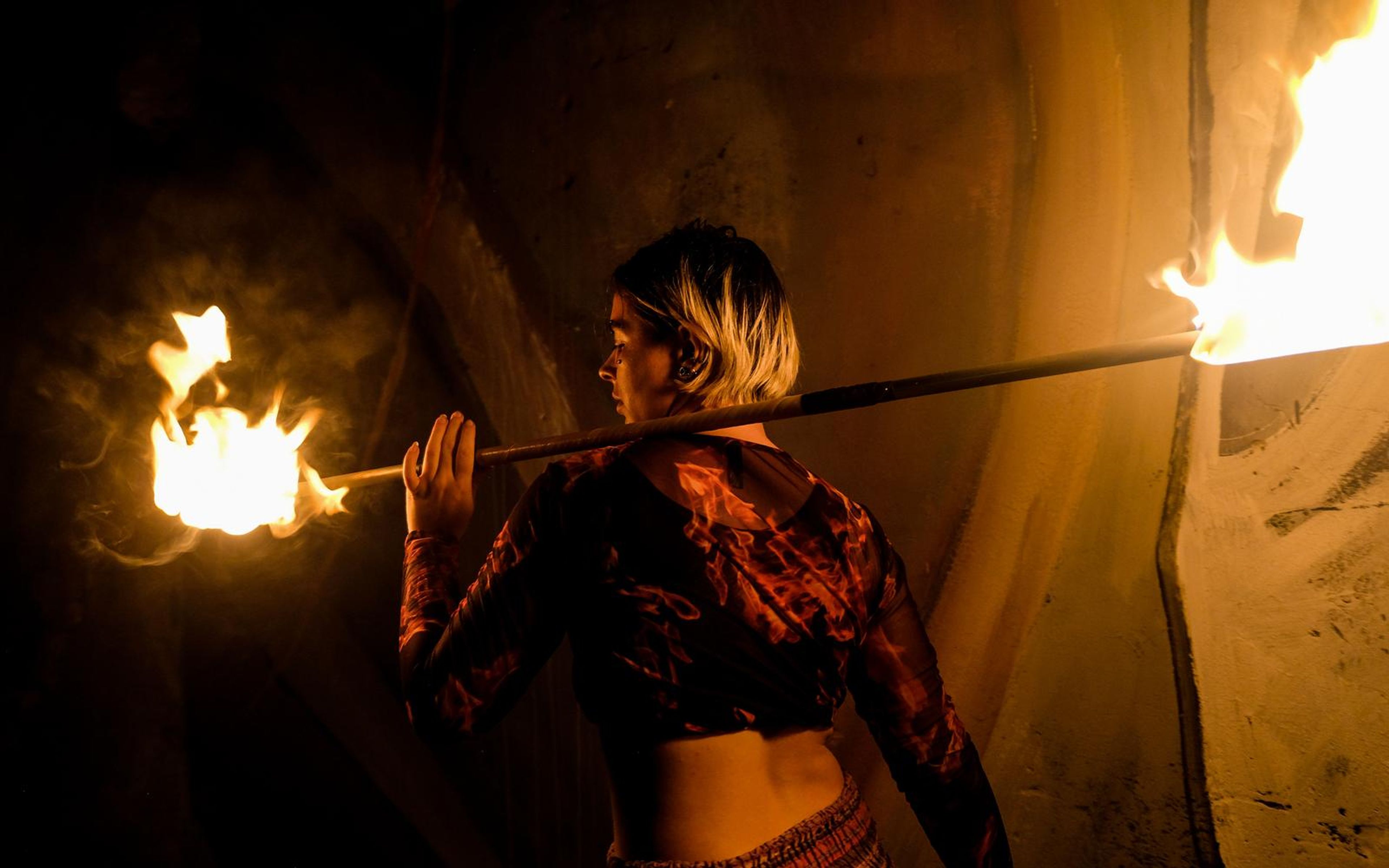 Orange-toned version of the performer from behind with a fire staff across the shoulders