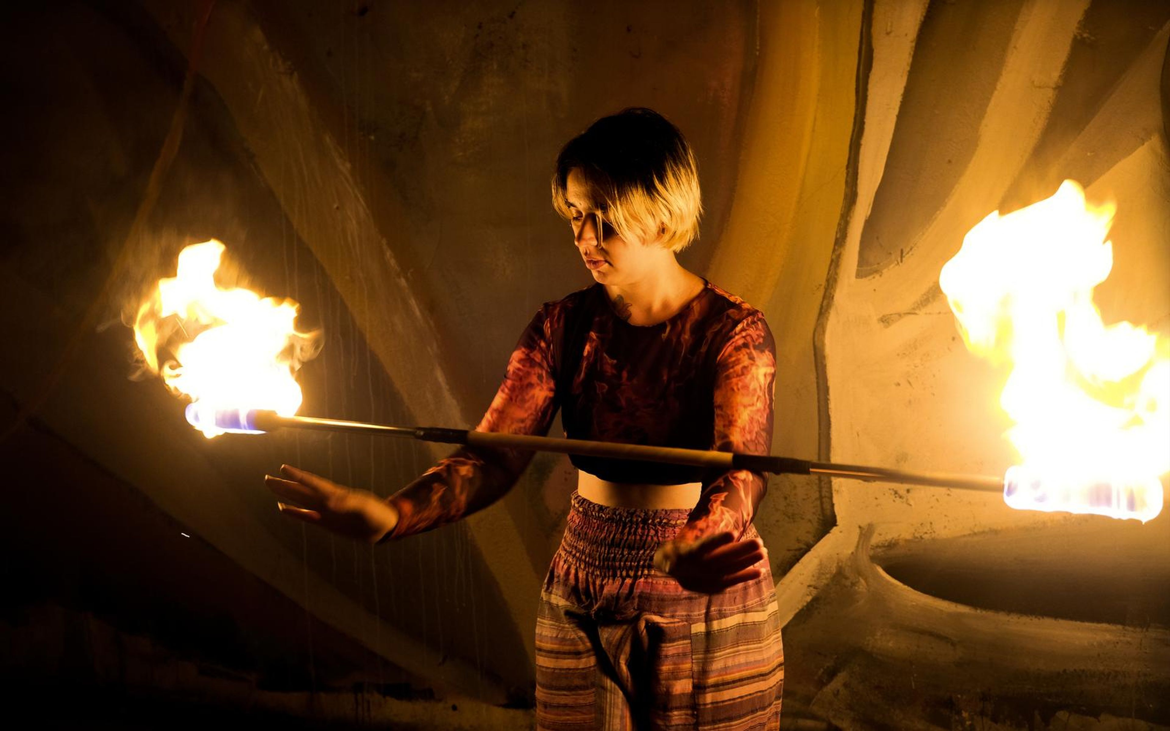 Closer view of a performer with a short blond haircut holding a fire staff with large flames at both ends