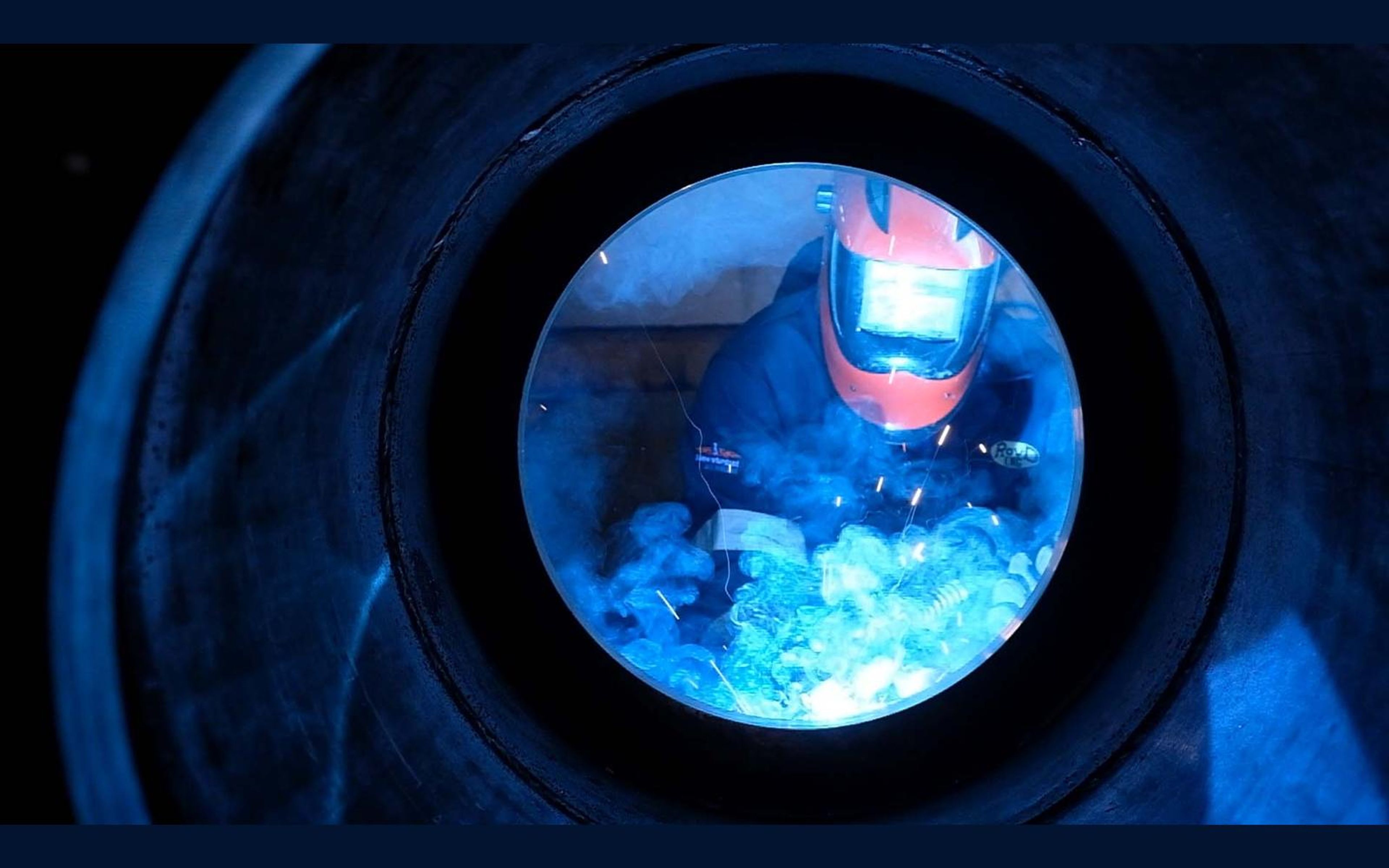 Welder seen through a round steel opening