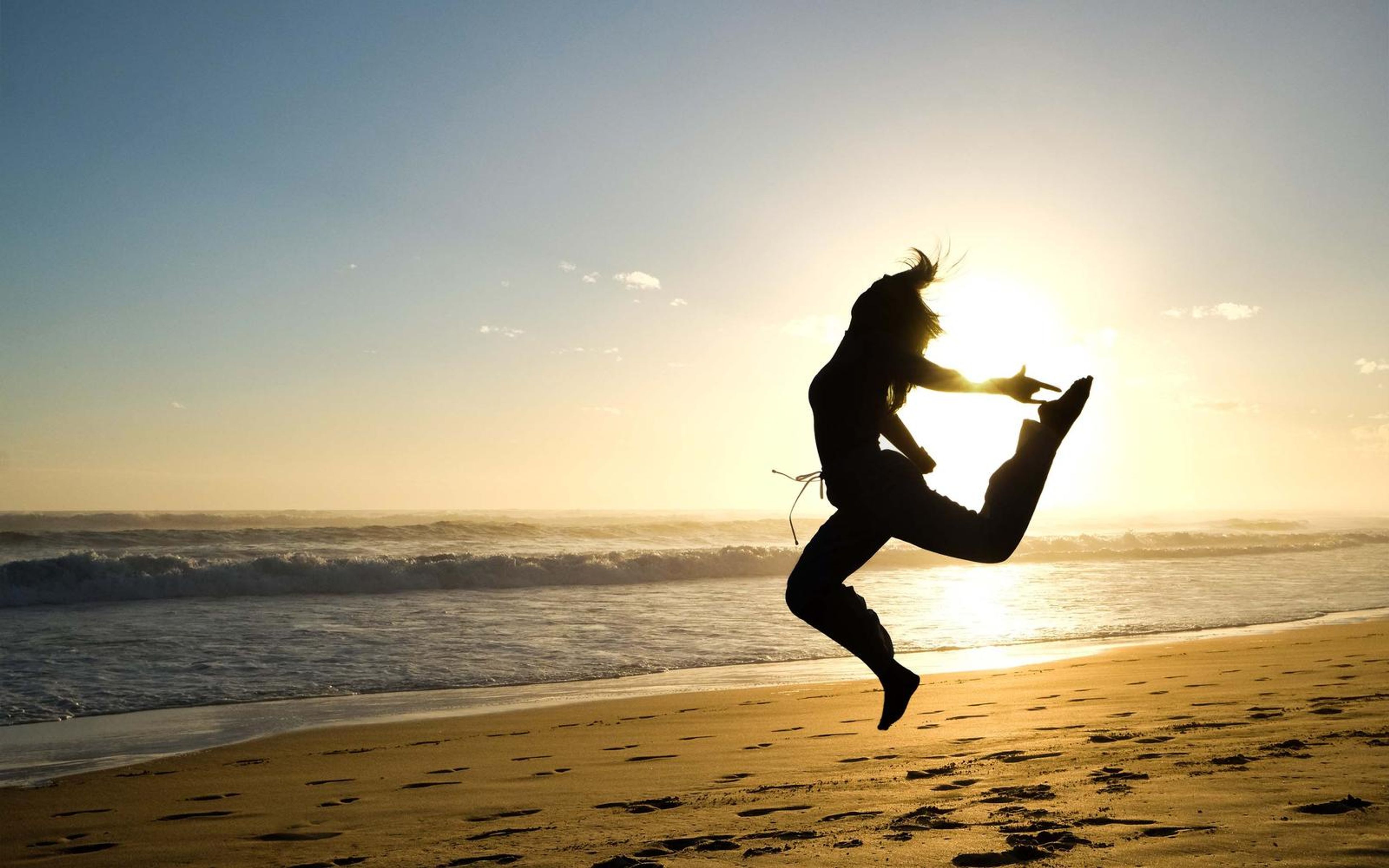 Silhouette of a woman jumping with legs split in the air above a sunset shoreline