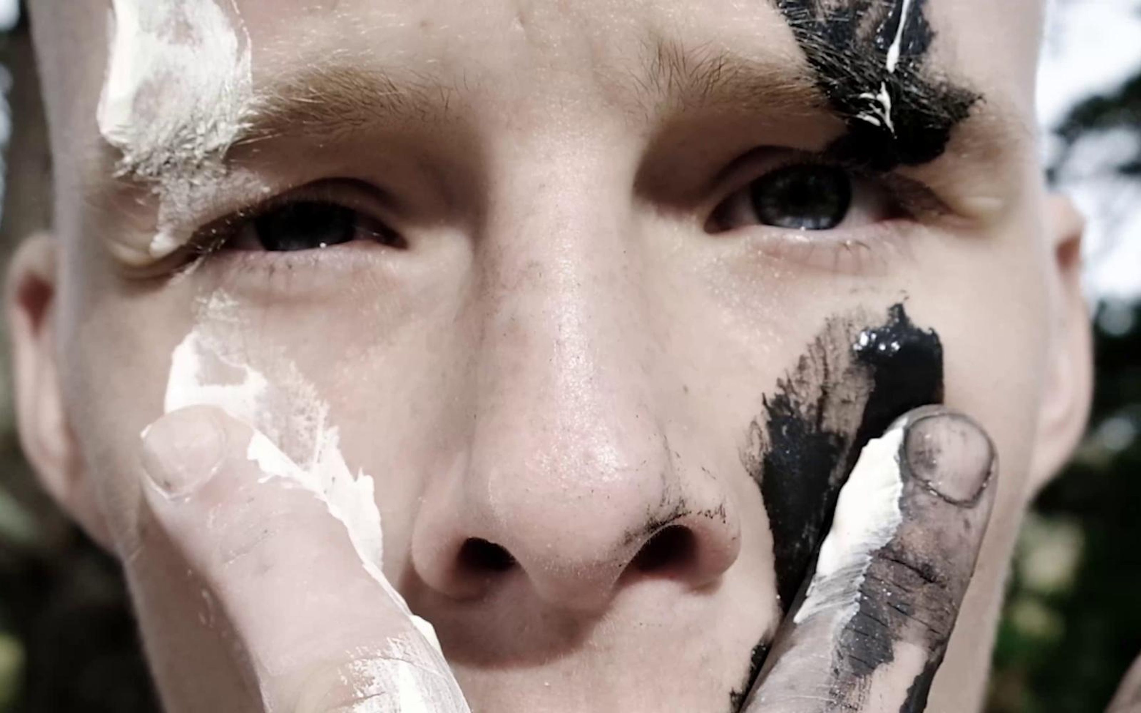 Close-up of the performer's face as he smears white paint beneath his eye