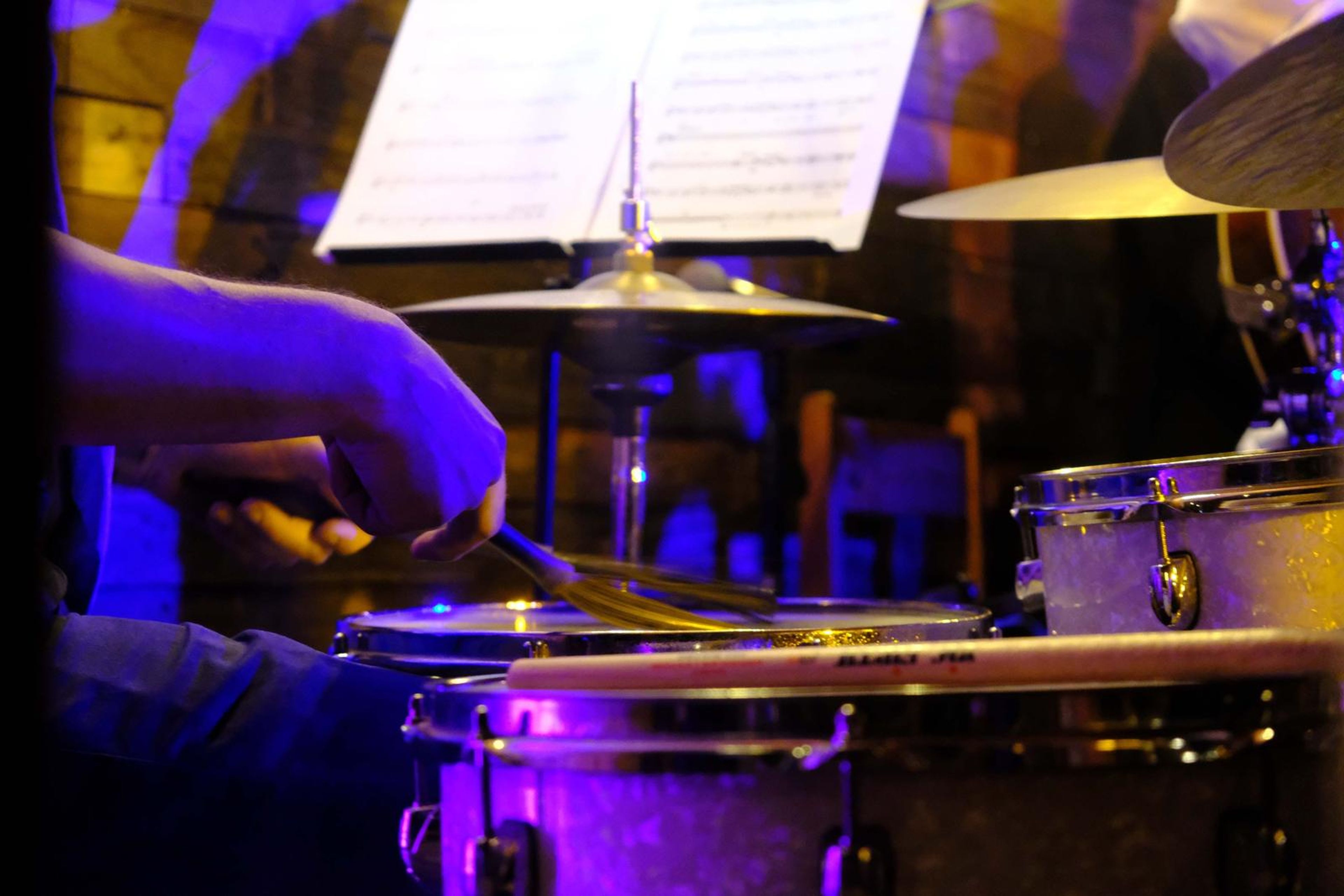 Close-up of the drummer's hands and cymbals under purple light