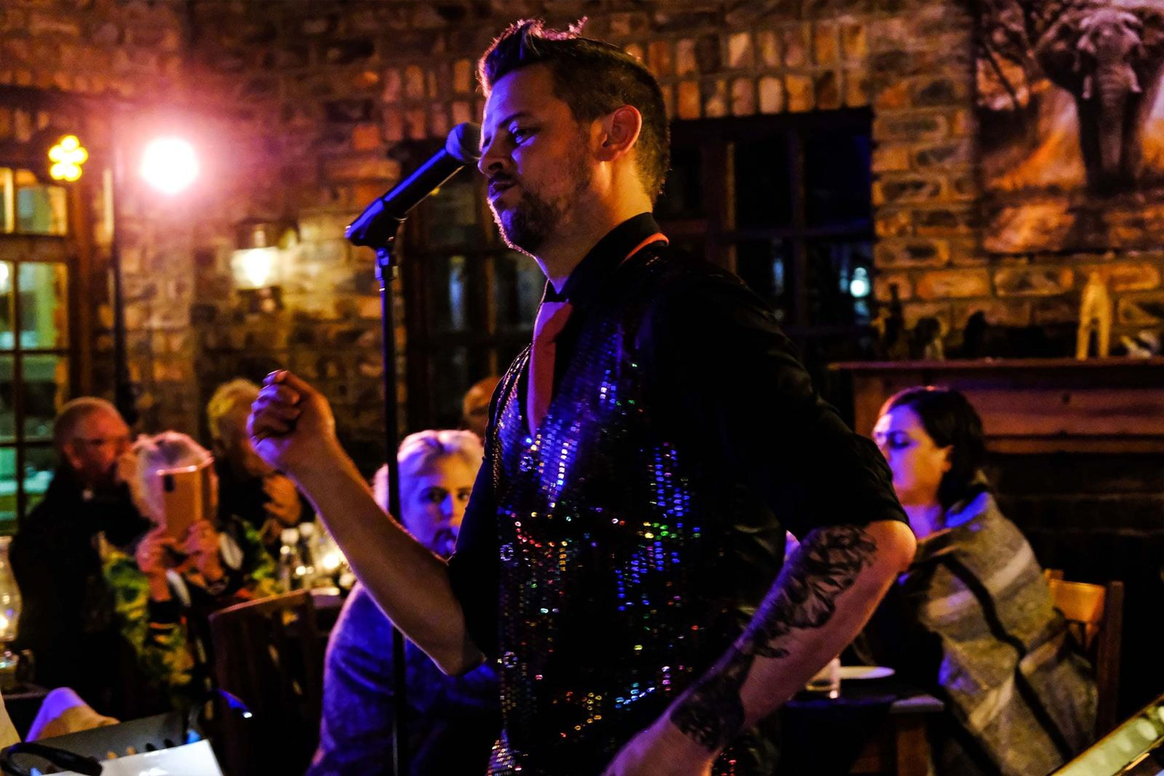 Lead singer in a sequin vest singing a line with a clenched fist among the diners