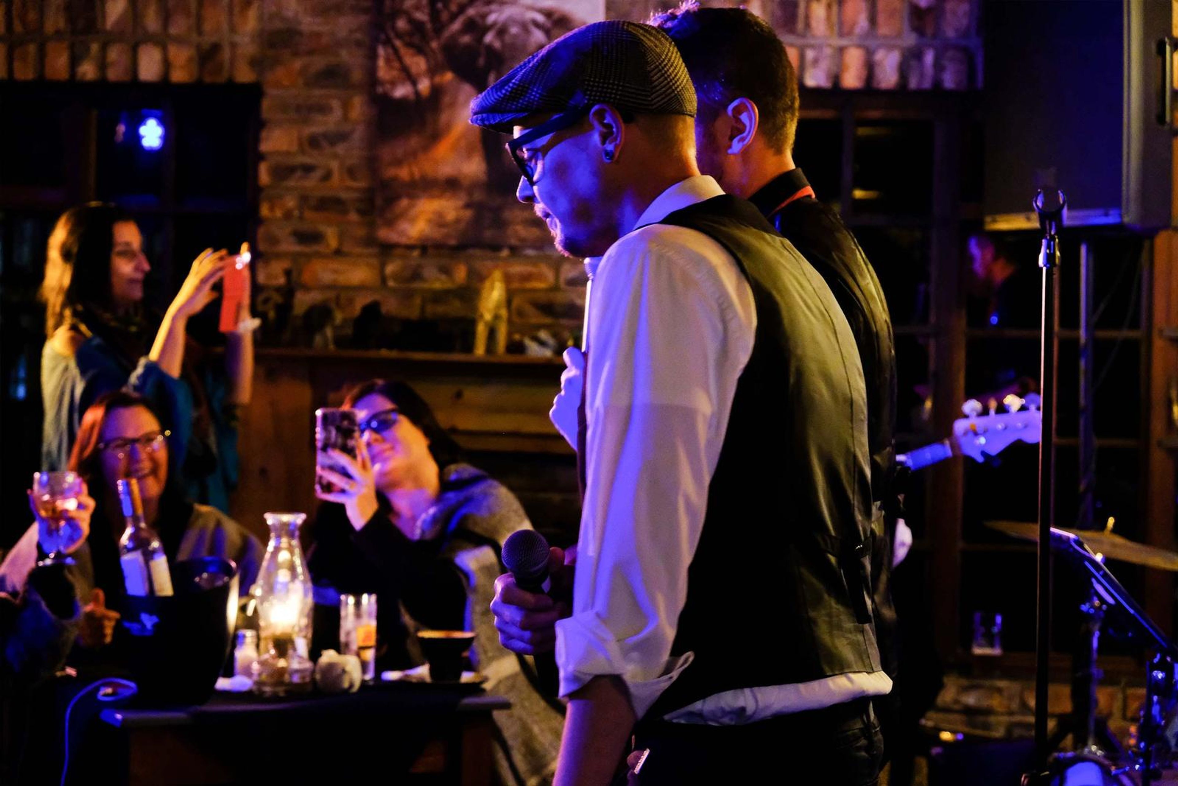 Singer in a flat cap walking through the room as guests raise their glasses