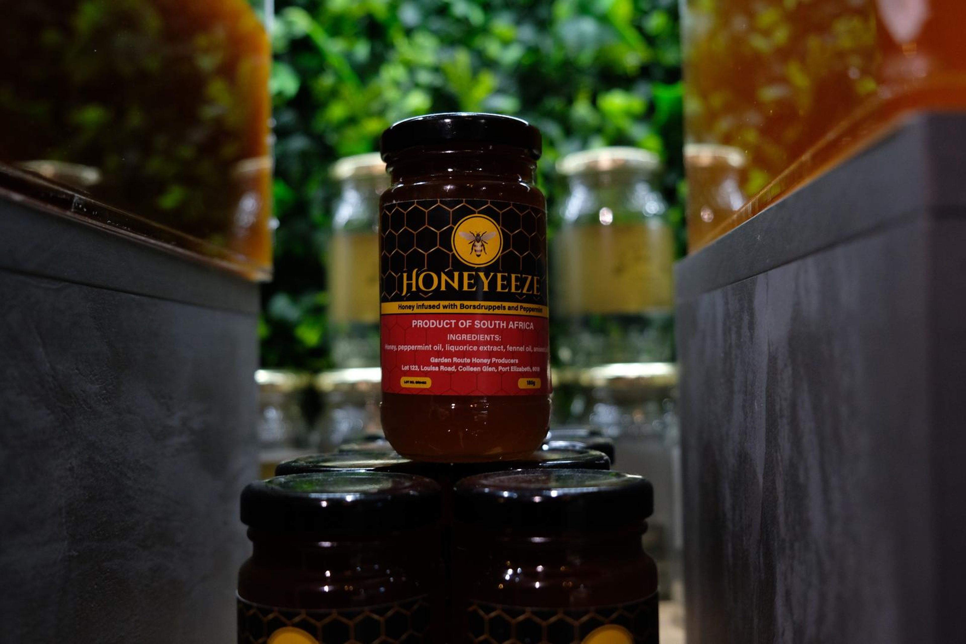 Honeyeeze honey jars on a slate stand in front of a green wall