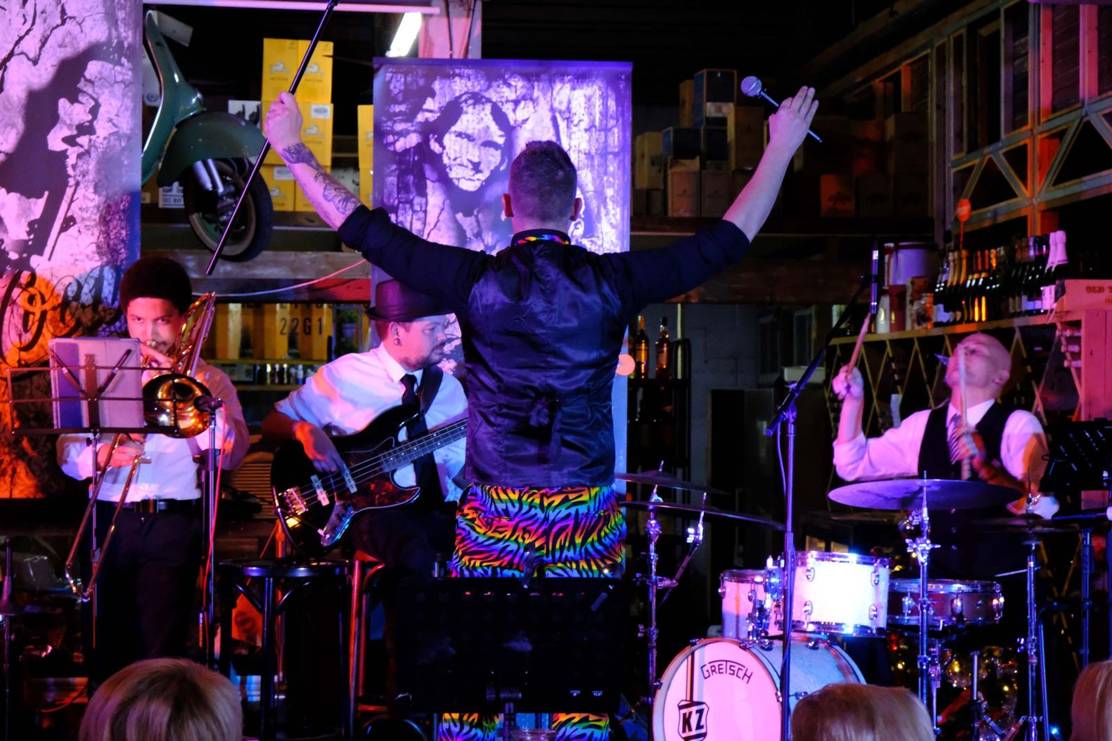 Singer with his arms raised, seen from behind, in front of a jazz mural
