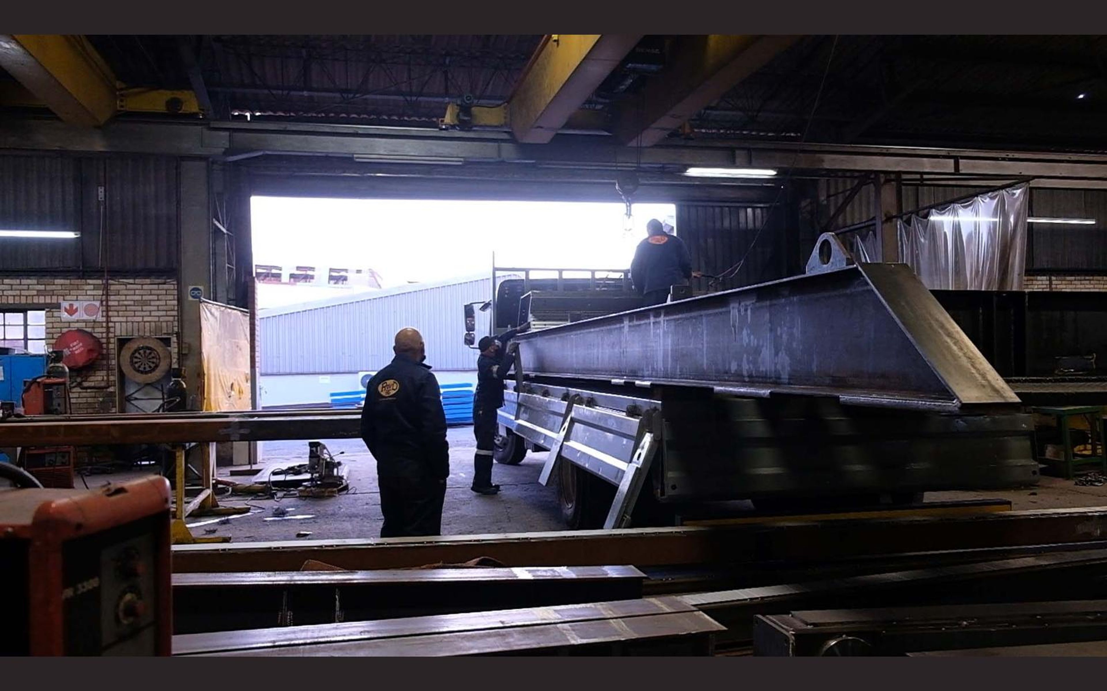 Fabricators at work among steel beams in the shop