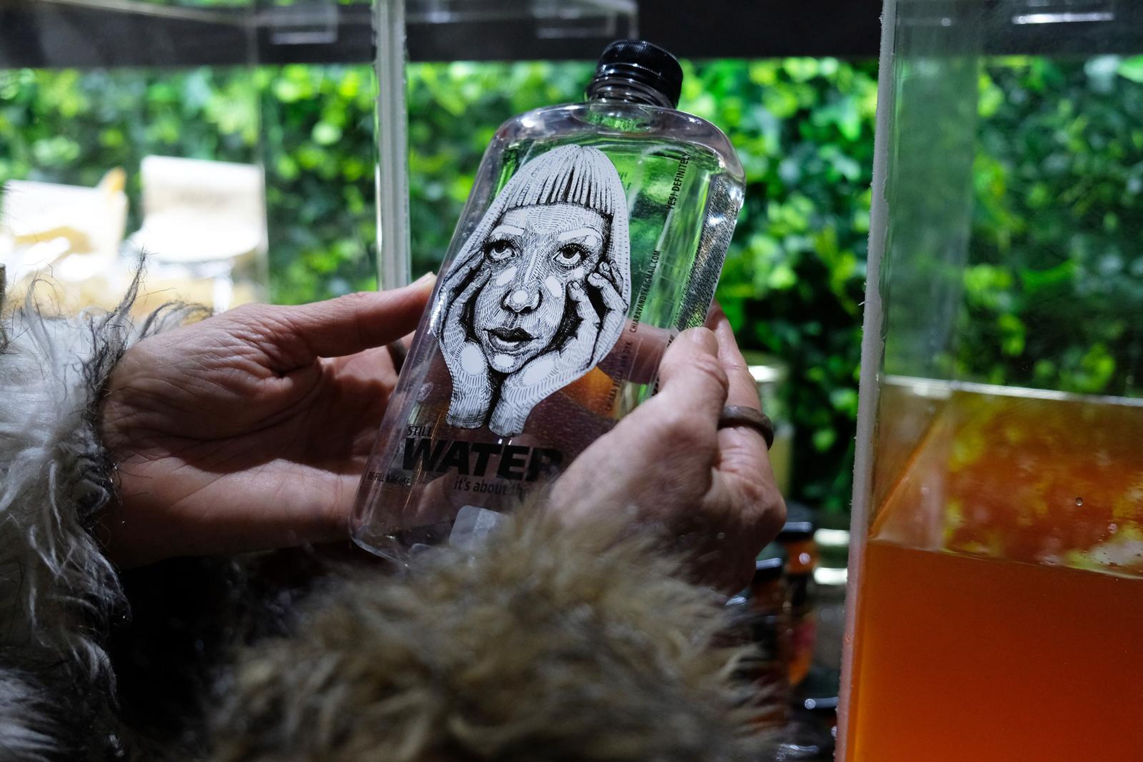 Close-up of a Water bottle with a hand-drawn portrait label against greenery