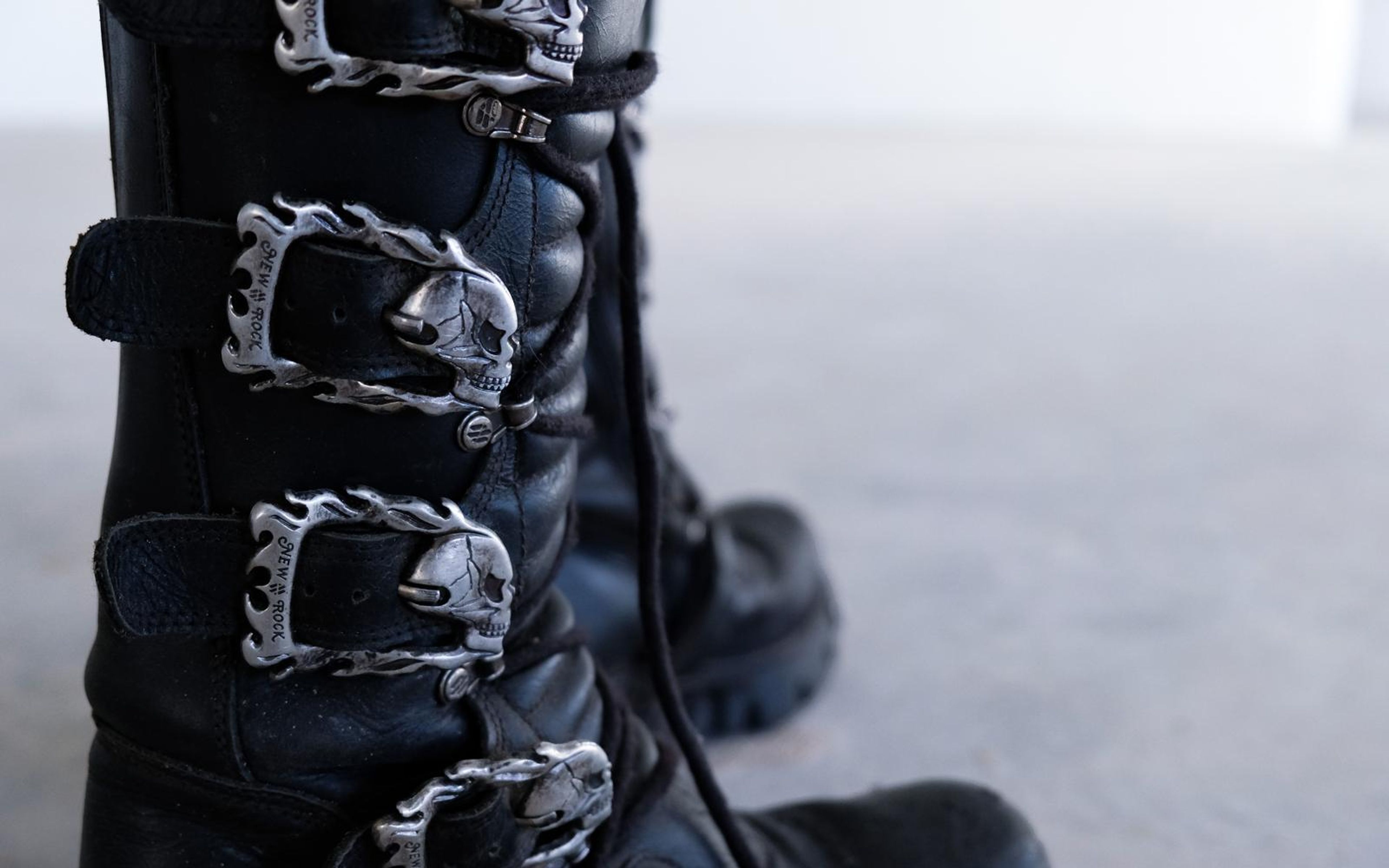 Extreme close-up of silver skull buckles and laces on a black boot, blurred concrete behind