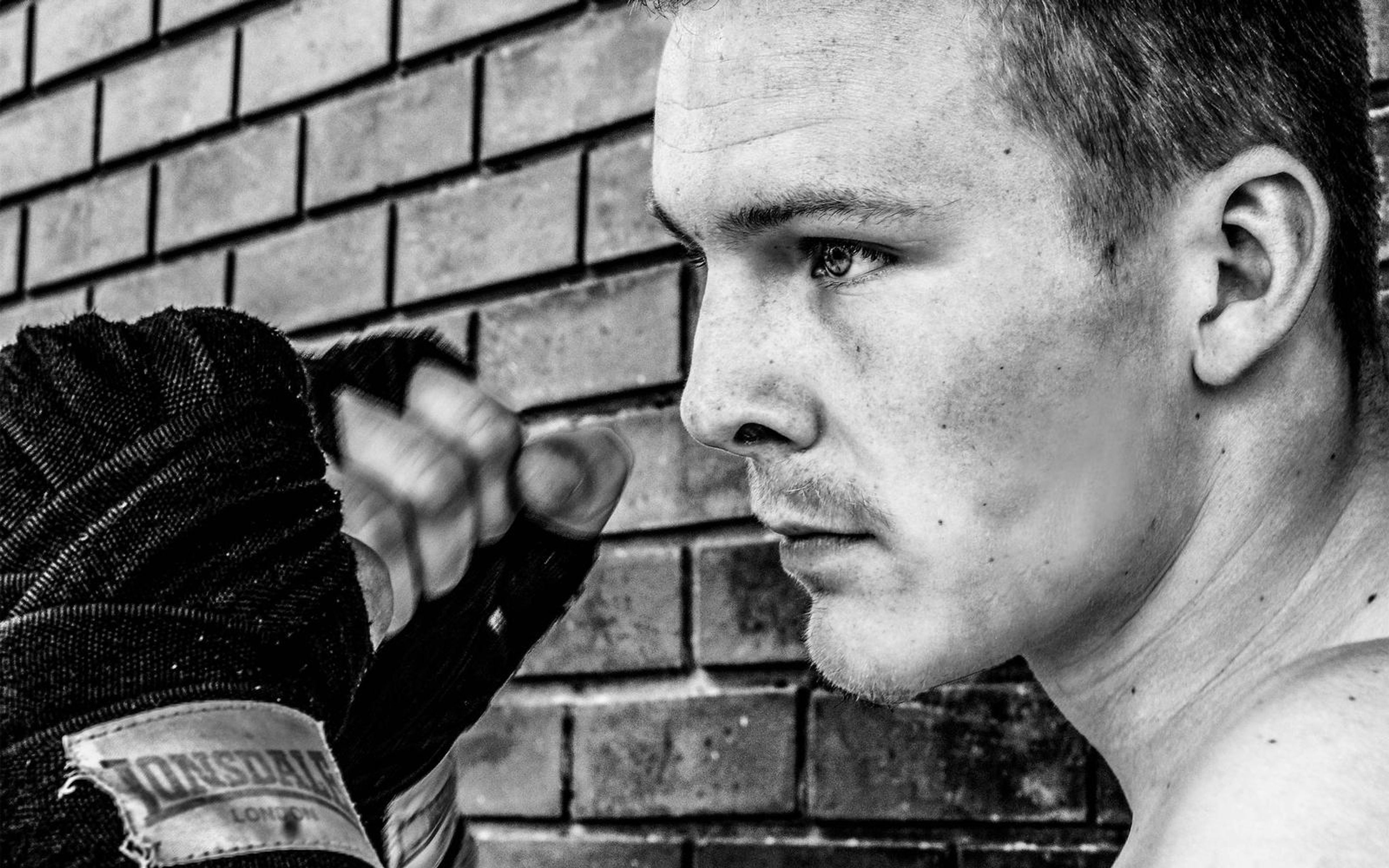 Black and white profile of the fighter with a wrapped fist in front of a brick wall