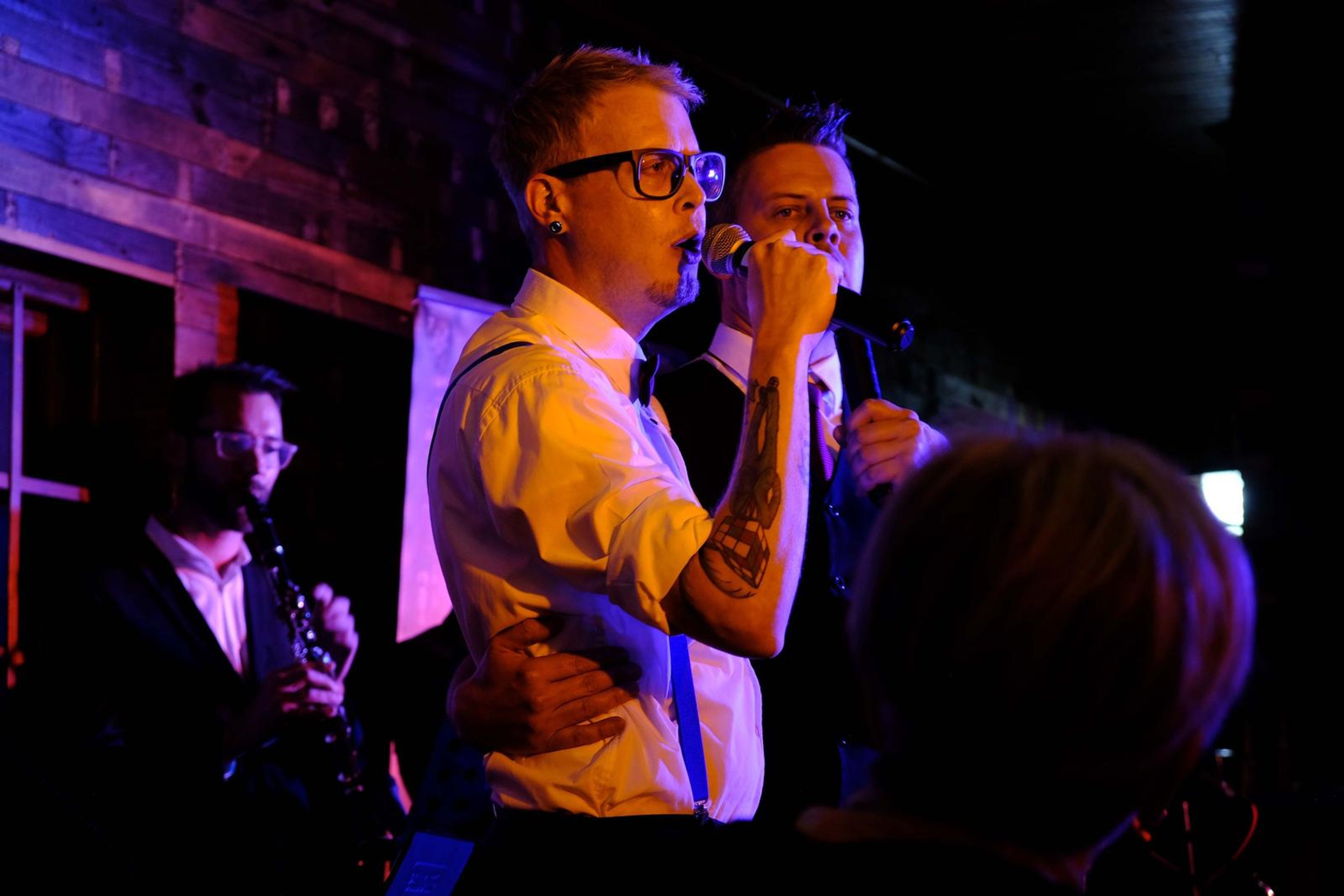 Two singers sharing the stage, one in suspenders and glasses
